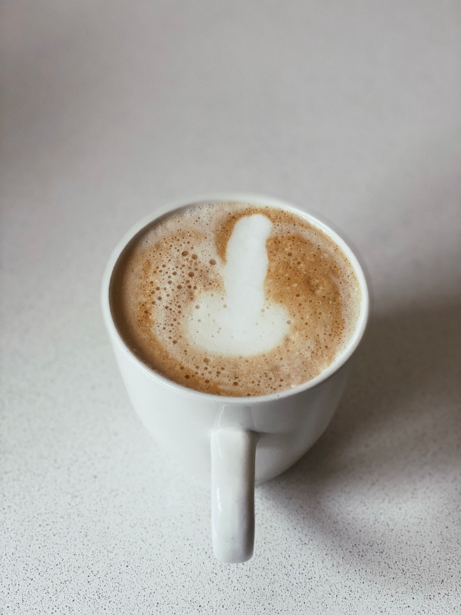 A photo of a mug of coffee with what very much looks like a penis and pair of testicles drawn in the froth at the top.