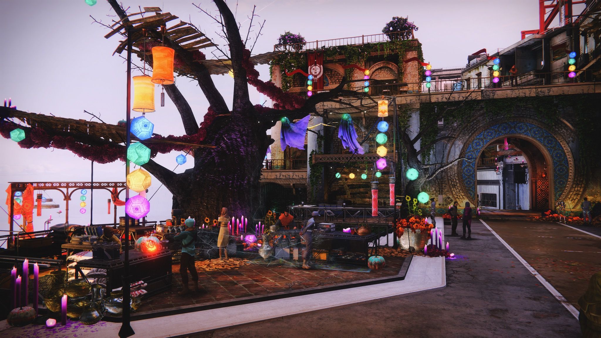A screenshot of one of the open areas in Destiny 2's "Tower" social space, with a big gnarled and dead tree in the middle, tall purple candles everywhere, along with some spiderwebs, jack-o-lanterns, and multicoloured geometric lights hanging from various points.