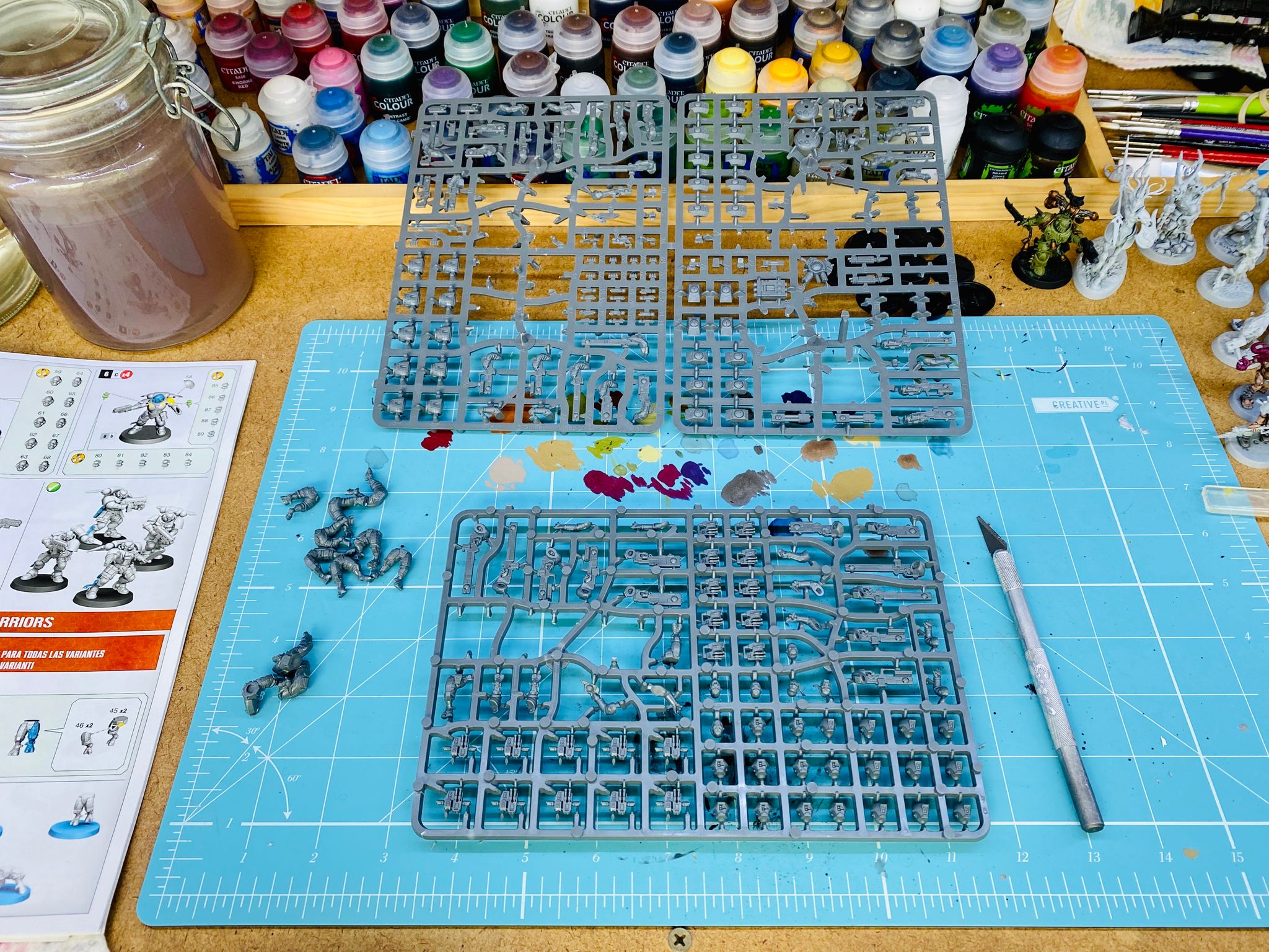 A photo of a desk with two plastic sprues with the contents of the Tau army from the Warhammer 40,000: Kill Team box set and a scalpel sitting next to them.