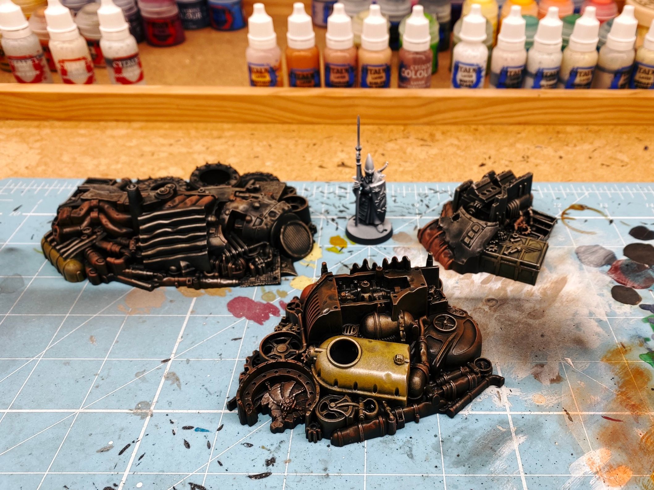 A photo of three of the terrain scrap/junk piles from the Warhammer 40,000 Kill Team: Octarius box that came out in July last year and has remained shamefully unpainted until now. They're all just a jumble of pipes and scraps of metal and fans and fuel tank and gears and such, and all are brown and worn and rusty-looking.