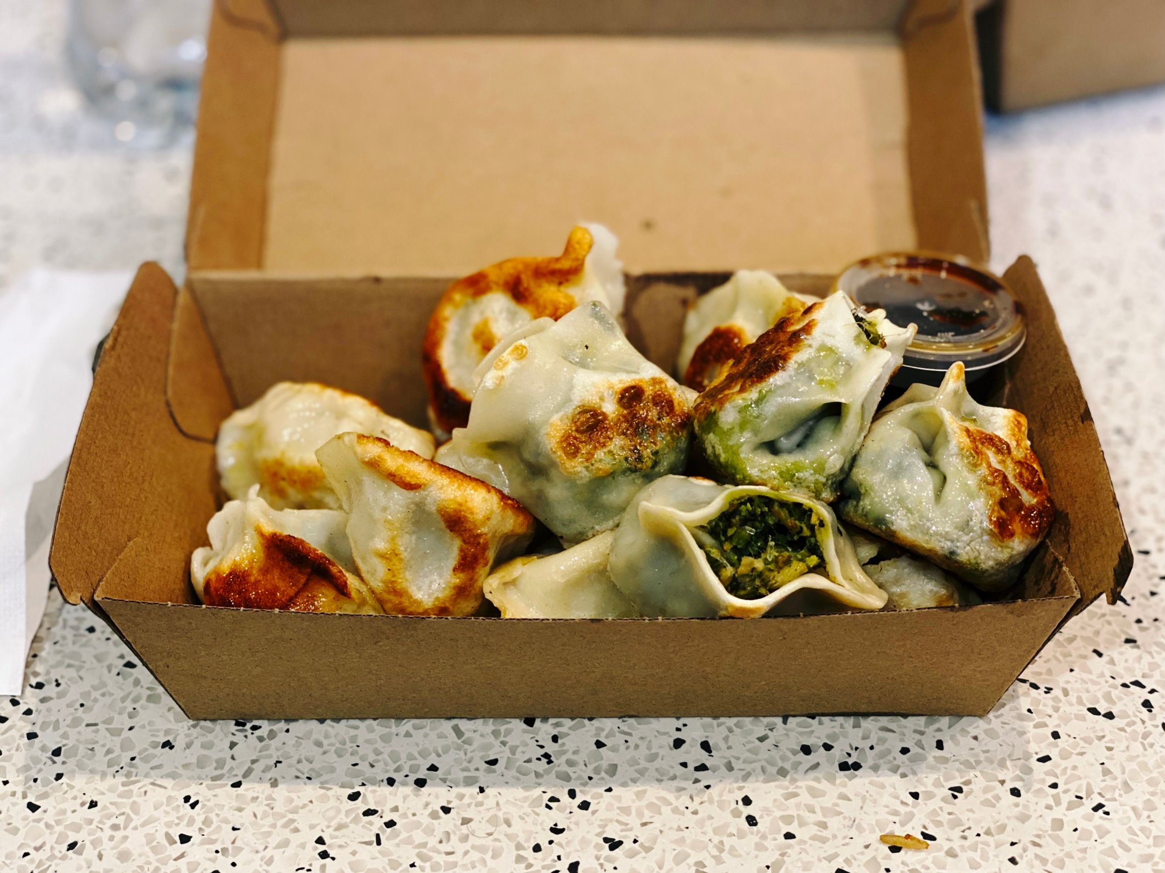 A photo of a pile of pan-fried dumplings in a cardboard takeaway box.