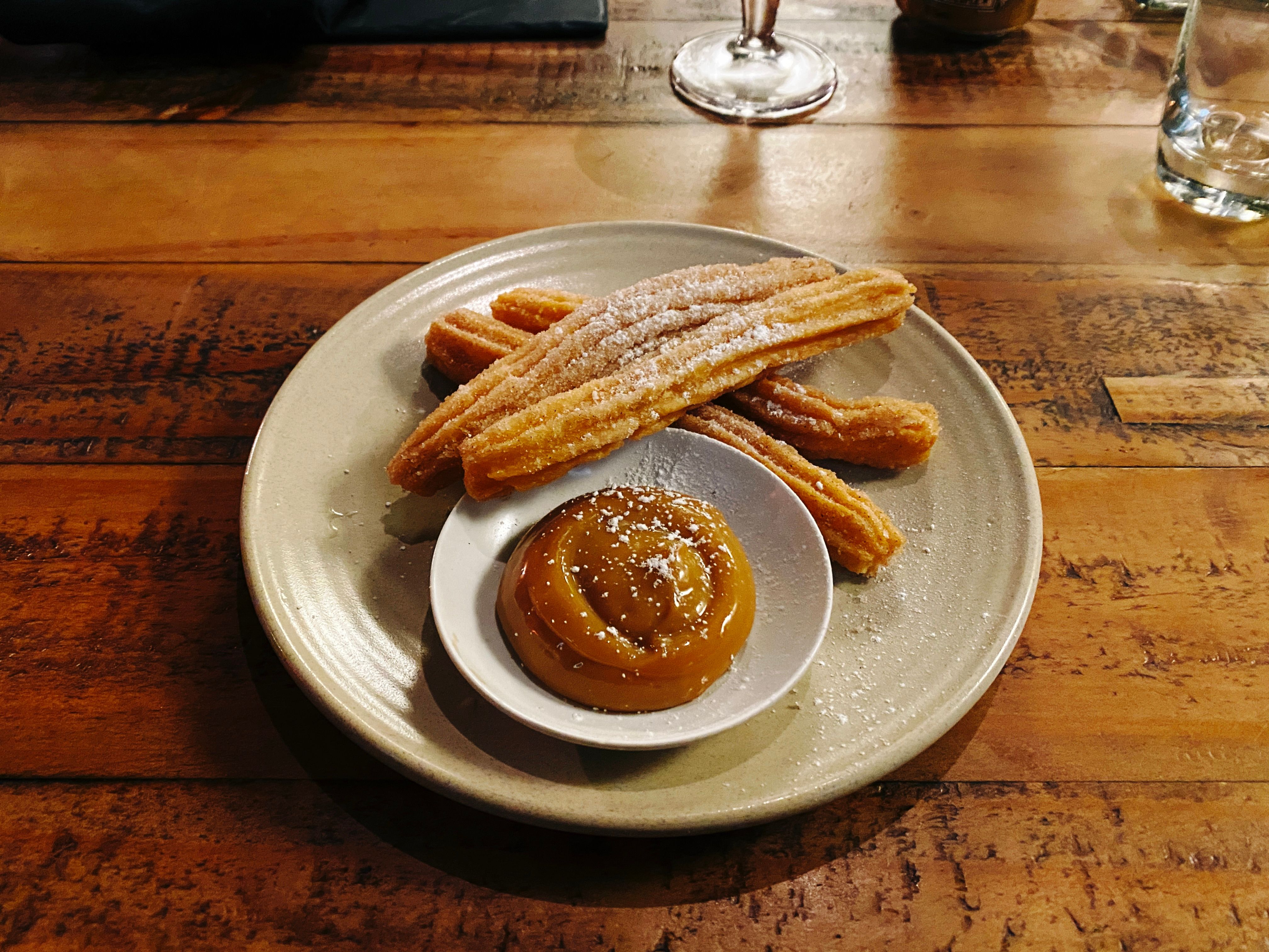 Four churros on a plate with a small saucer of dulche de leche.
