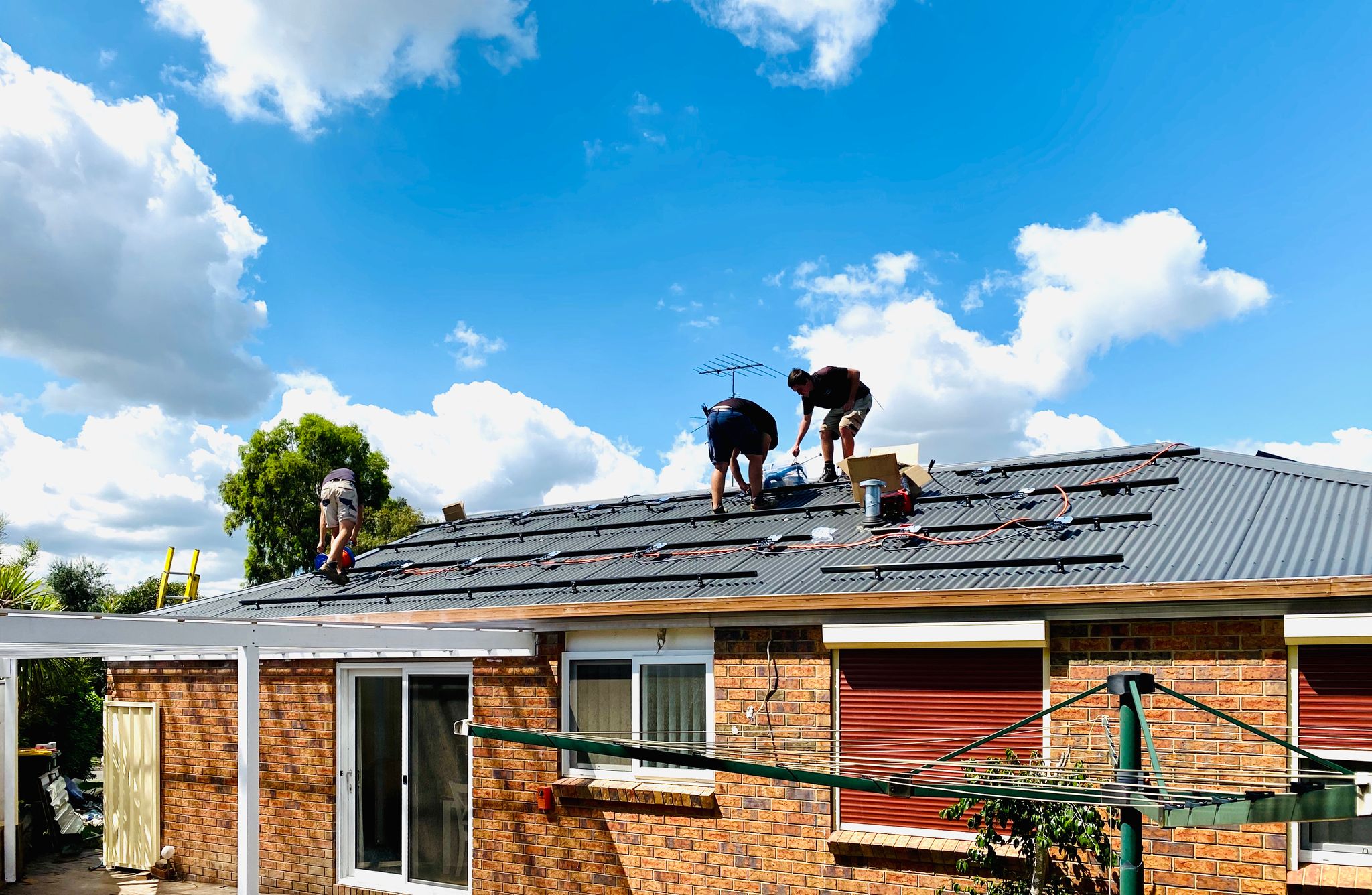 A photo of three tradies standing on our roof, with a set of sturdy-looking mounting rails having been attached to it.