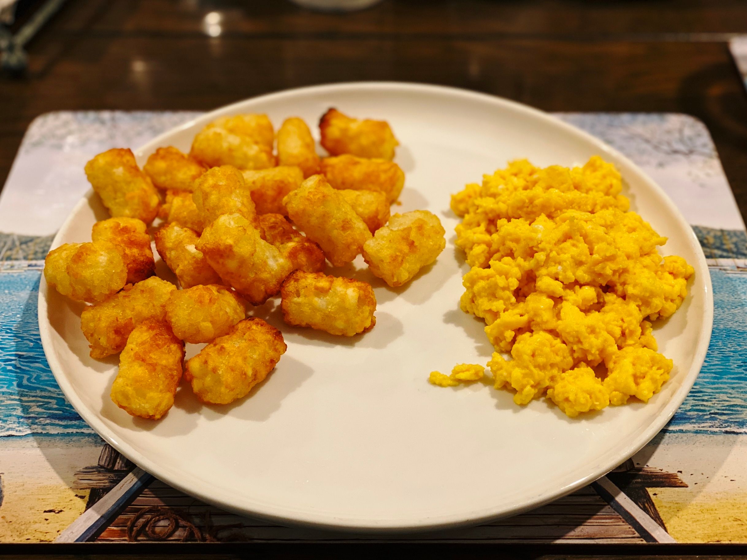 A photo of scrambled eggs and potato gems sitting on a plate. The potato gems are golden-brown and crispy, and the eggs are fluffy.