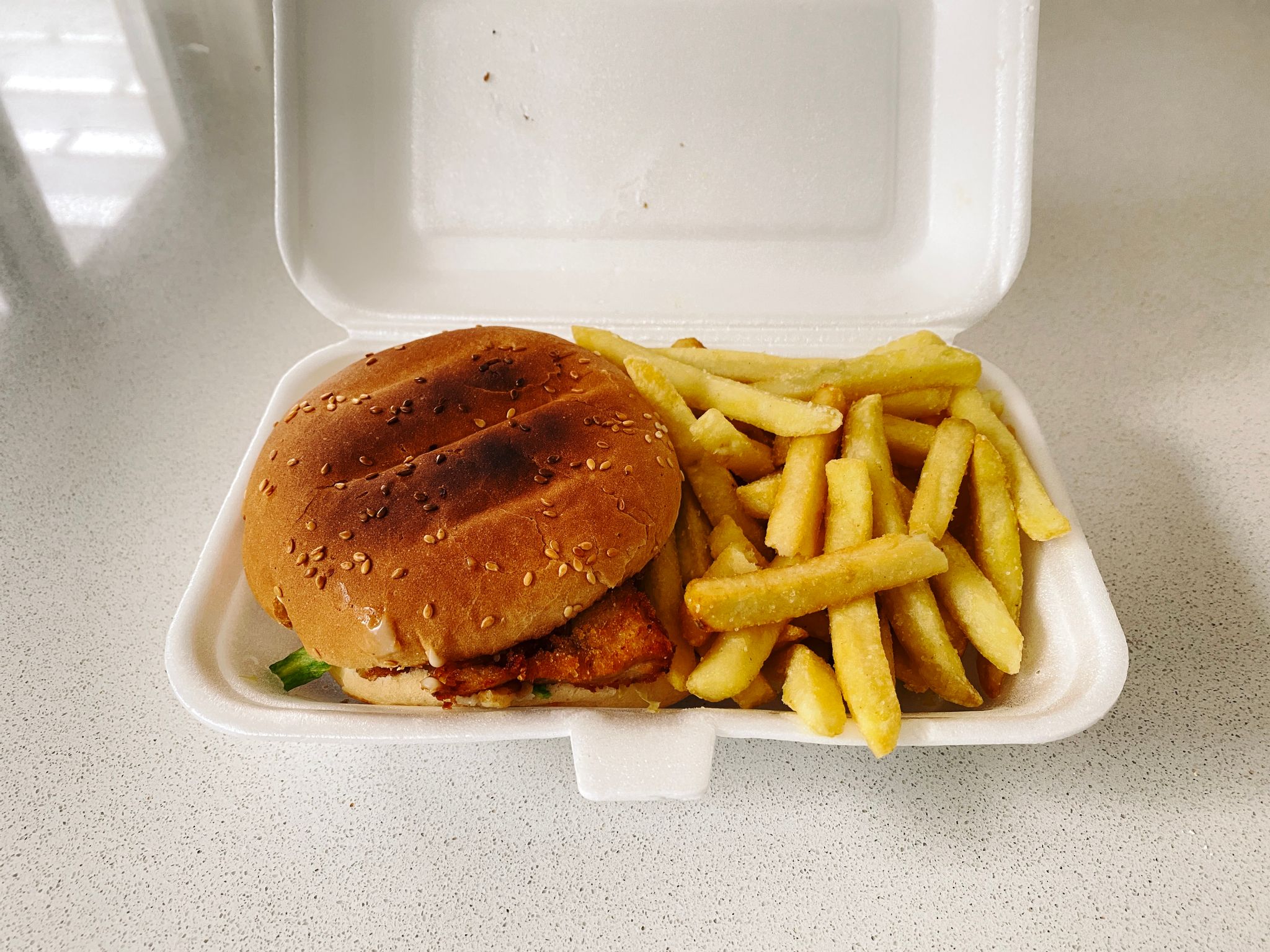 A photo of a chicken burger and chips in a polystyrene takeaway food container.