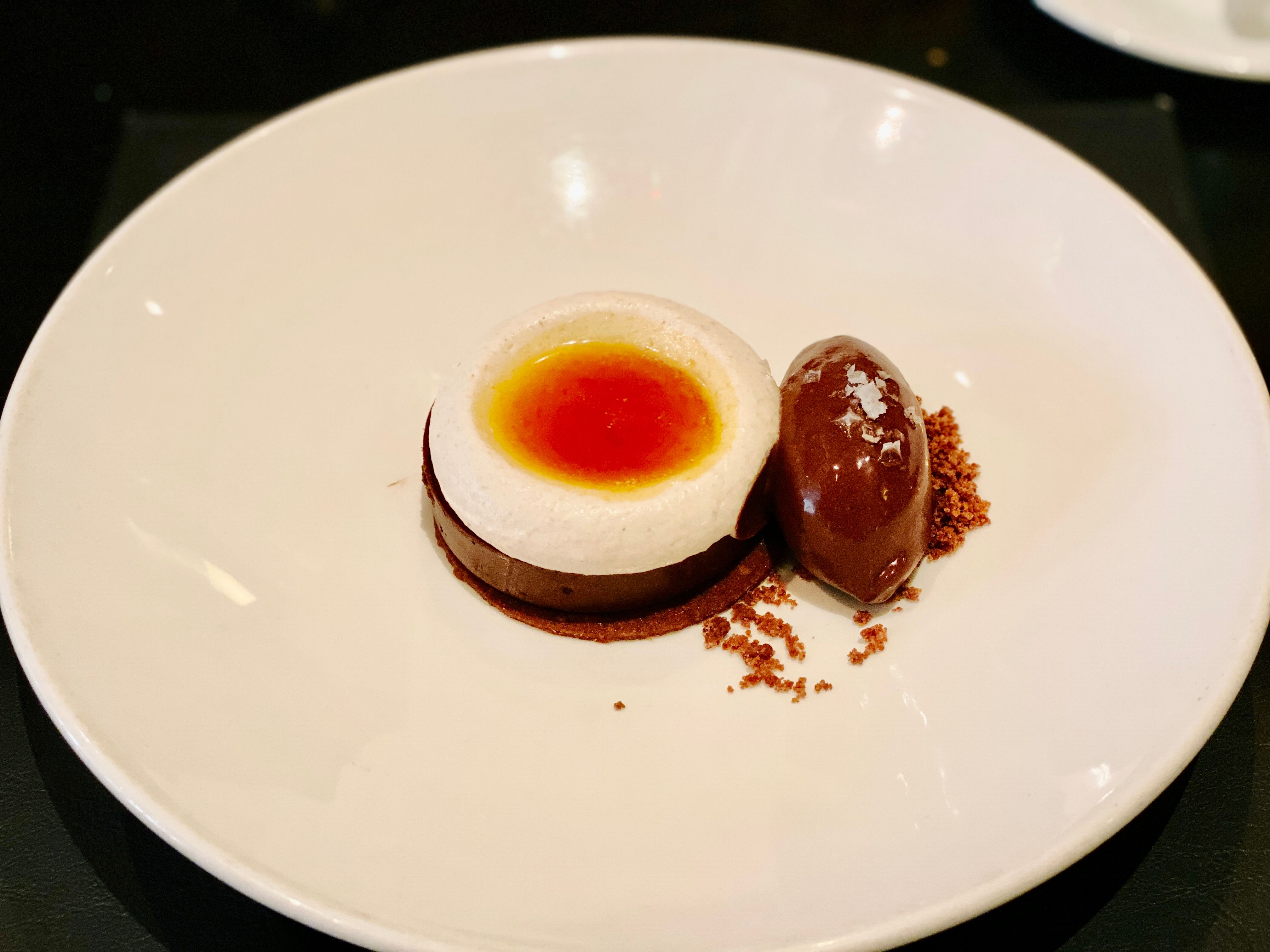 A photo of a chocolate marquise with cream on top like it's a little shallow cup, and whiskey caramel pooled inside the cream. Next to it is some chocolate sorbet.