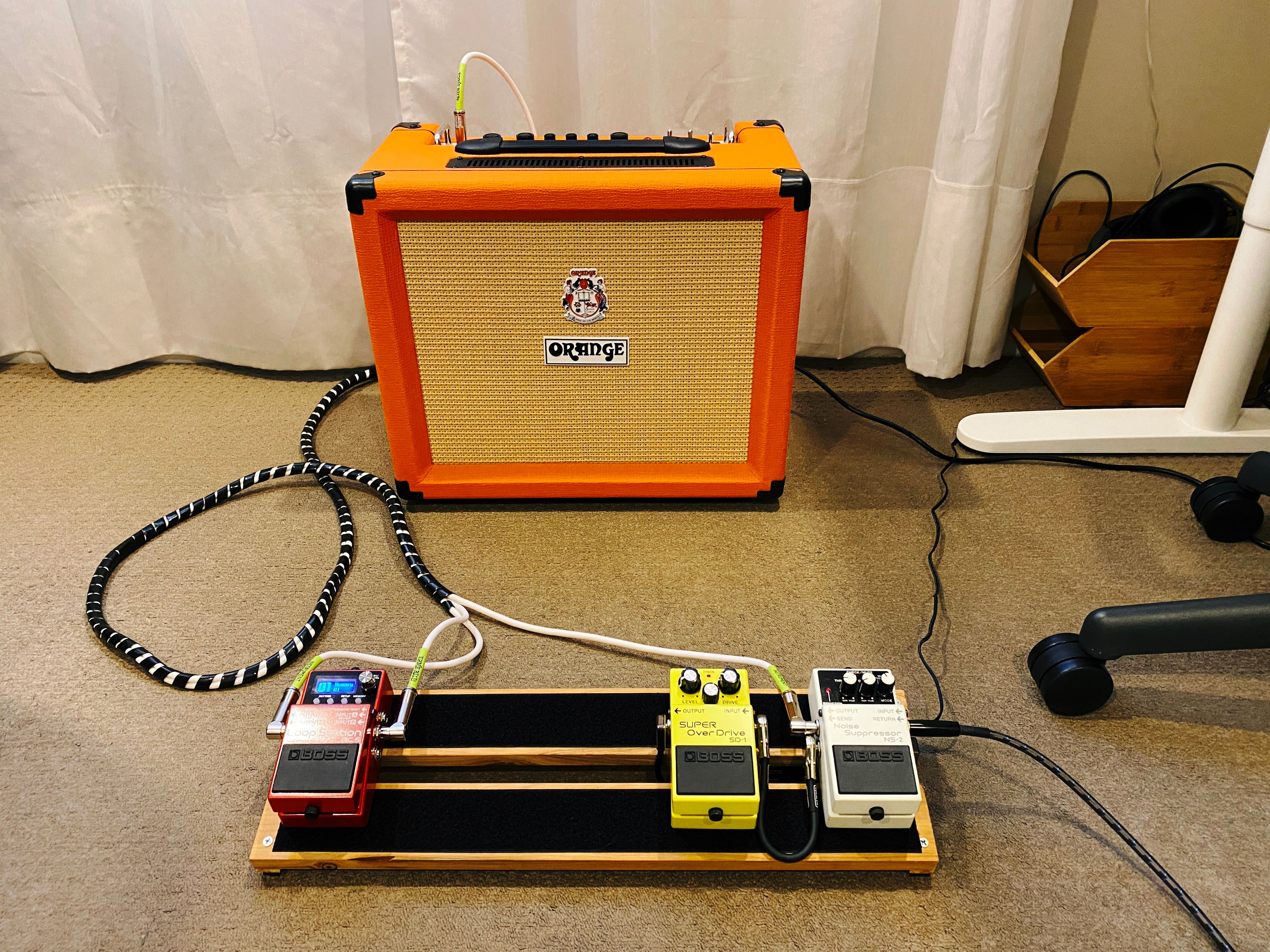 A photo of the pedalboard sitting in front of an Orange (and coloured orange) guitar amplifier.