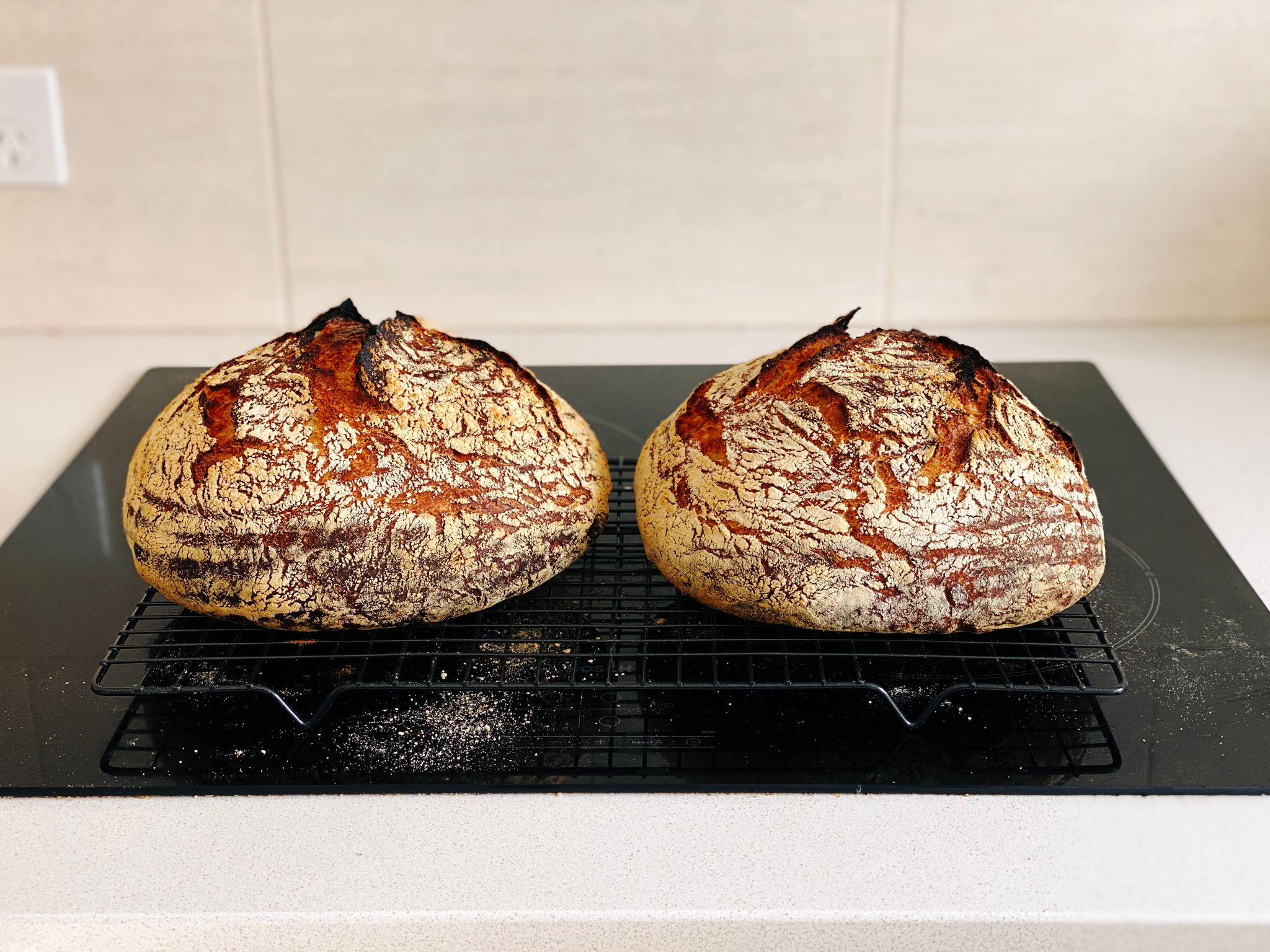 A photo of two brown loaves of bread sitting on a cooling rack.