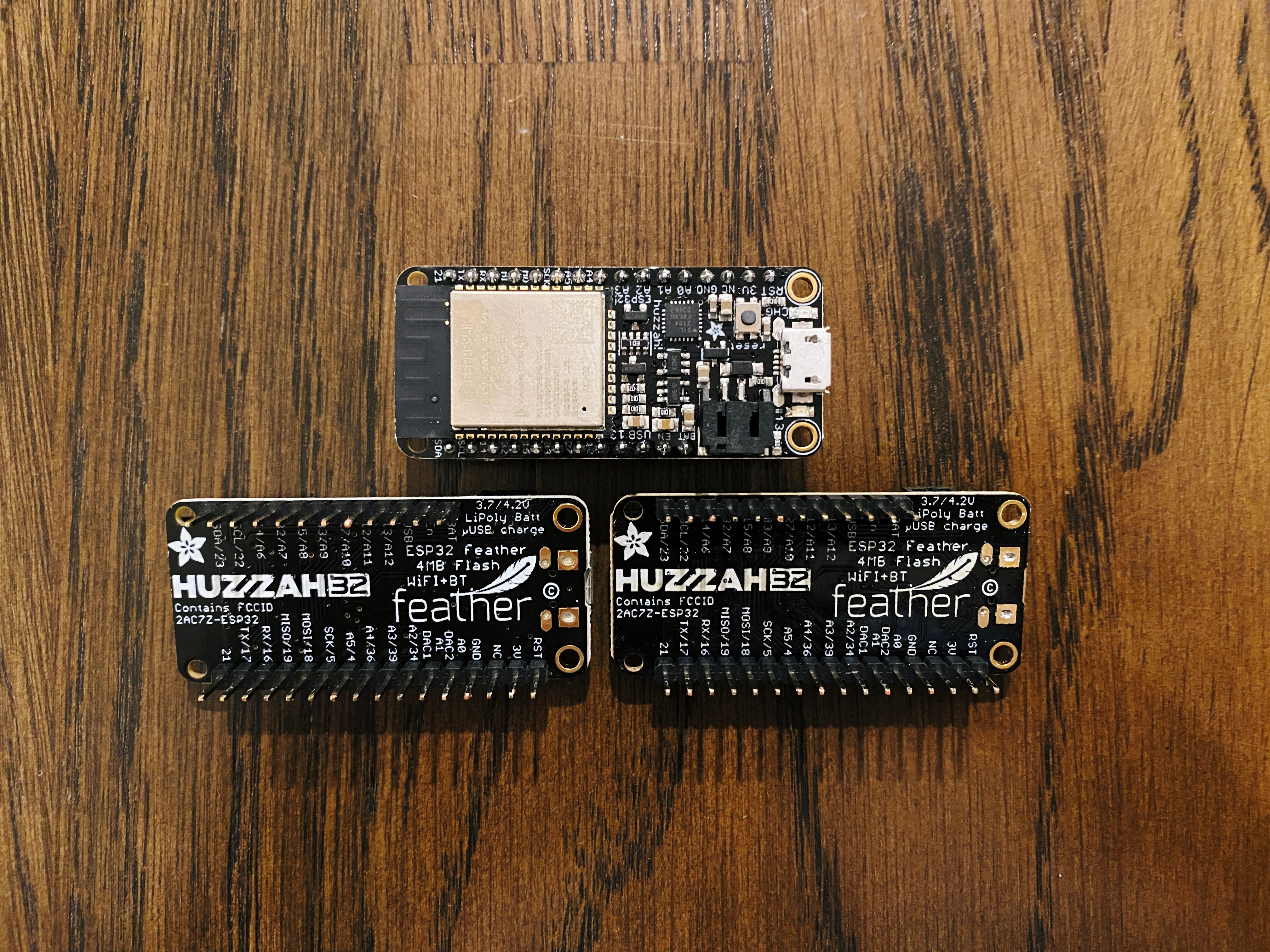 A photo of three ESP32 microcontrollers. They're teensy little circuit boards, roughly 5cm in length and 2cm in width, festooned with electronic components, and with two rows of pins coming out of them on one side for plugging things thing.