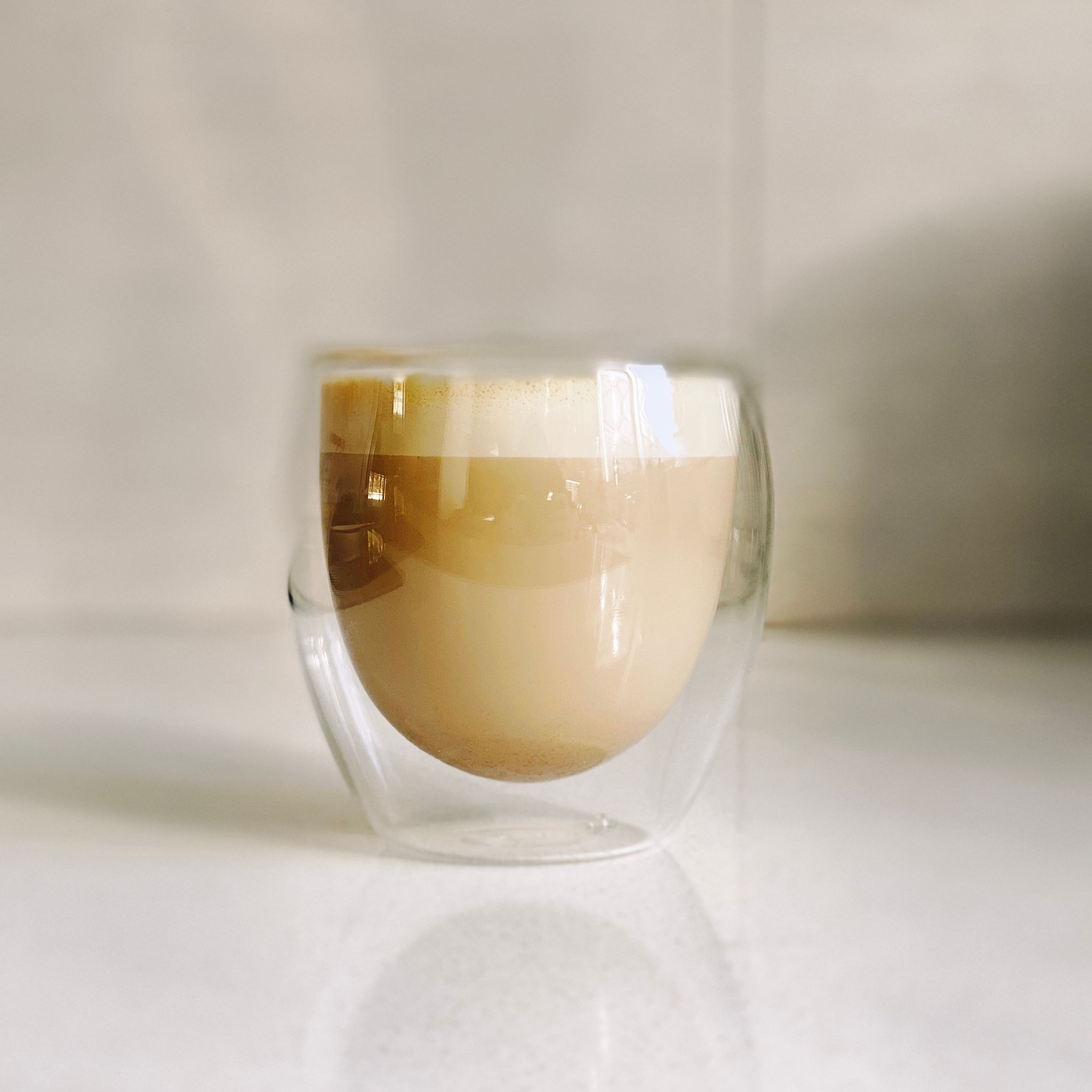 A photo of a double-walled curved coffee glass with a milk-based espresso in it, with a bit of foam on the top.