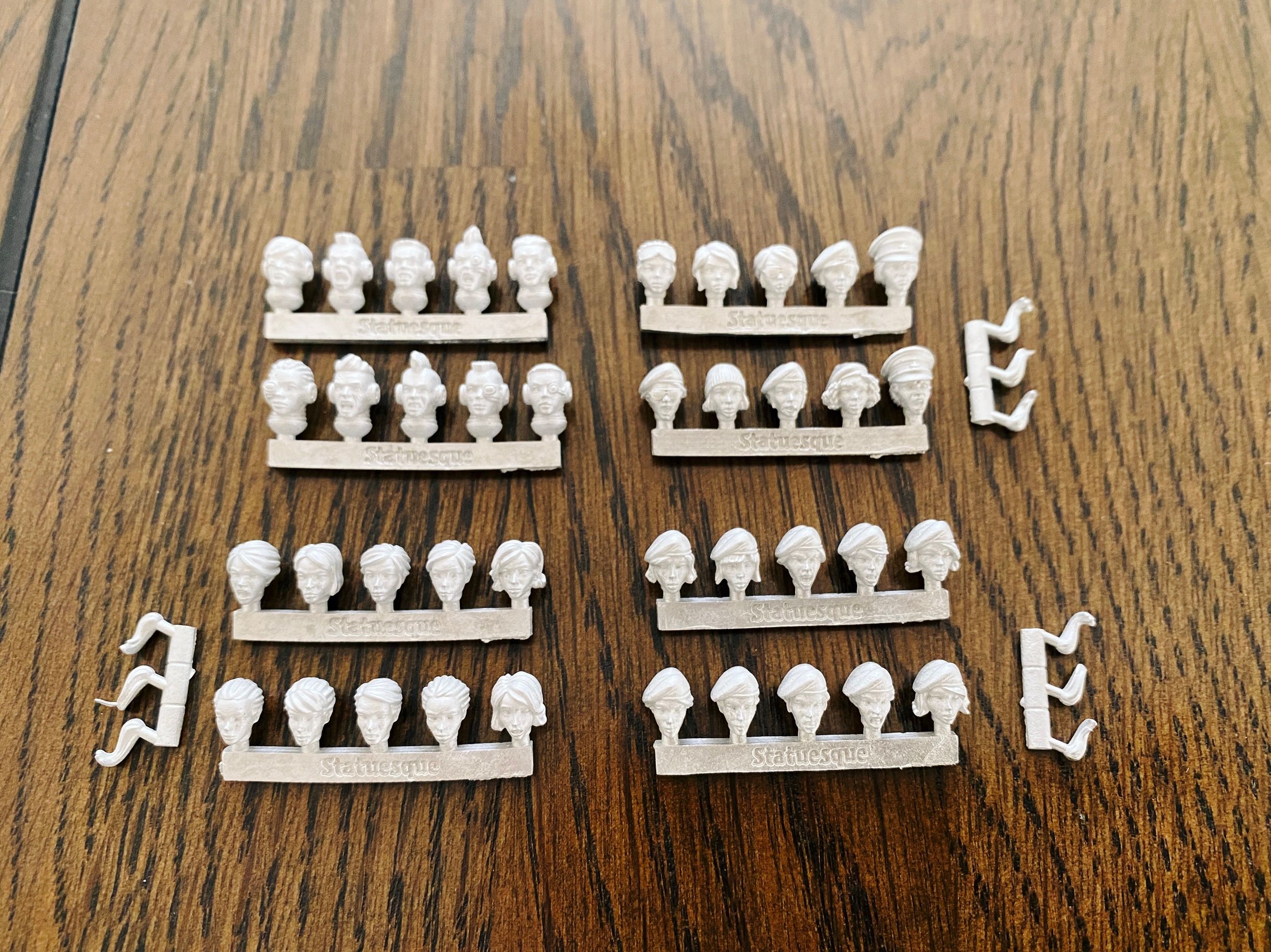 A photo of four sets of ten female heads for Warhammer 40,000-sized miniatures. One set has mohawks and cybernetic implants, one has a selection of "grizzled veteran" headgear like a beret, a beanie, sunglasses, one has a cigar, etc. The third set all have berets on, and the last have no headgear at all.