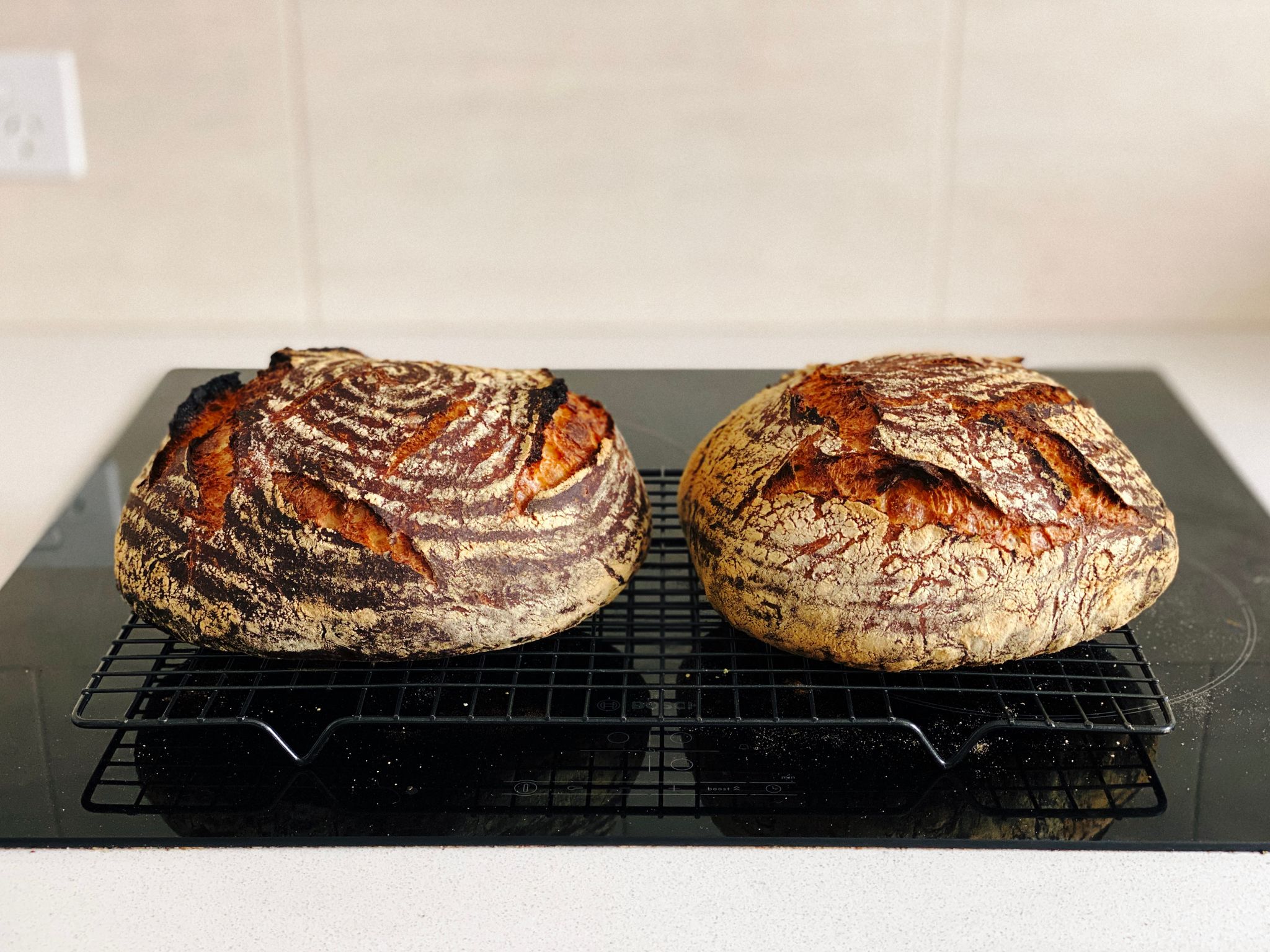 A photo of two round dark brown loaves of bread sitting on a cooling rack.