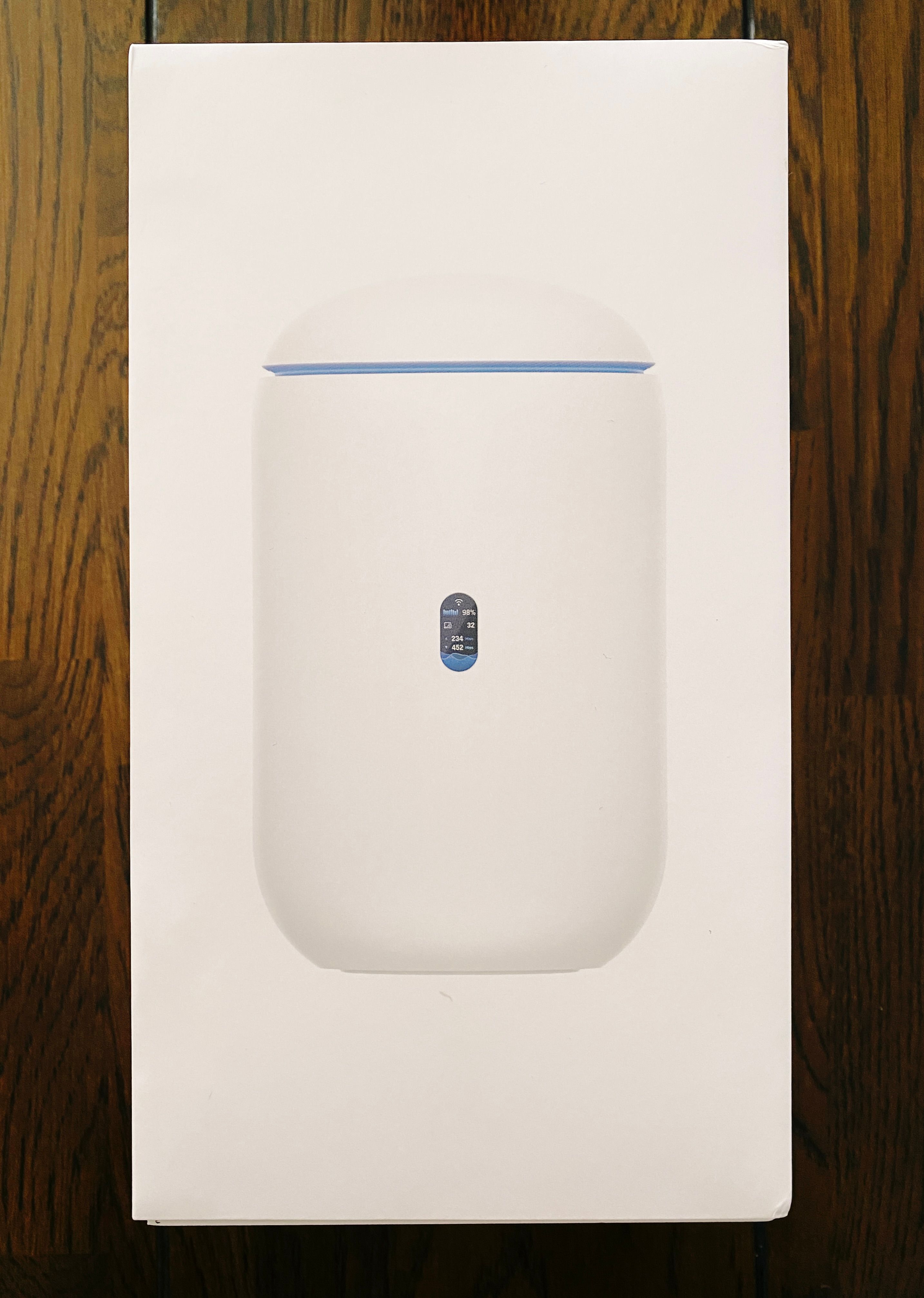 A photo of the box of the Dream Router. The router itself looks like a little squat white cylinder with a ring around the top and a gently curved top and bottom.