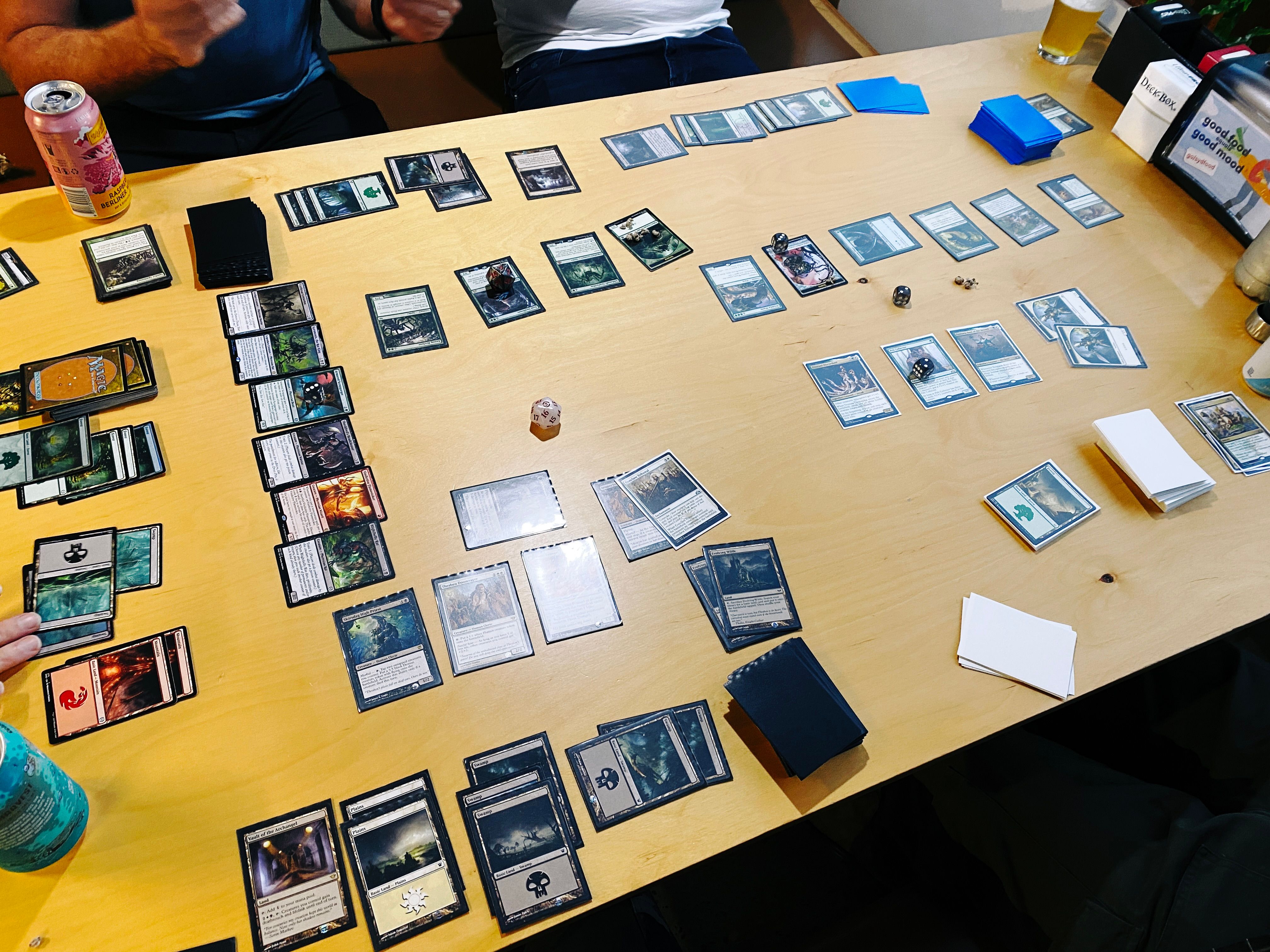 A photo of an in-progress five player game of Magic the Gathering, with cards all over a table.