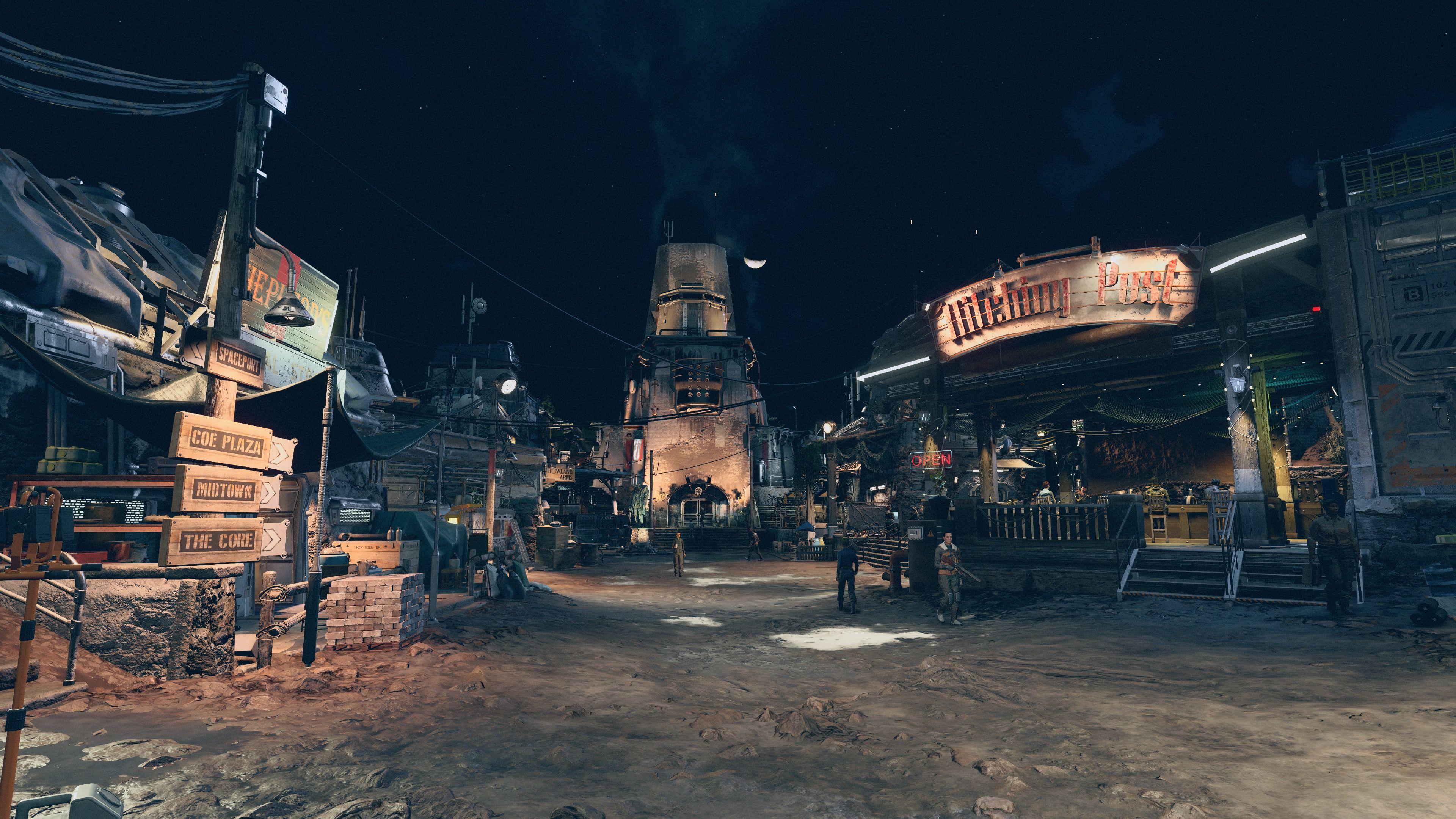 A screenshot taken from person-level at the entrance of Akila City, during the night. It's got a very wild west sort of feel to it, the ground is dirt and the buildings are cobbled together out of a combination of wood and futuristic-looking metal. It's not very well lit and the lights are quite yellow-coloured. In the centre of the frame is an imposing-looking multi-storey mostly built out of stone, with more yellow lights lighting it up from below.