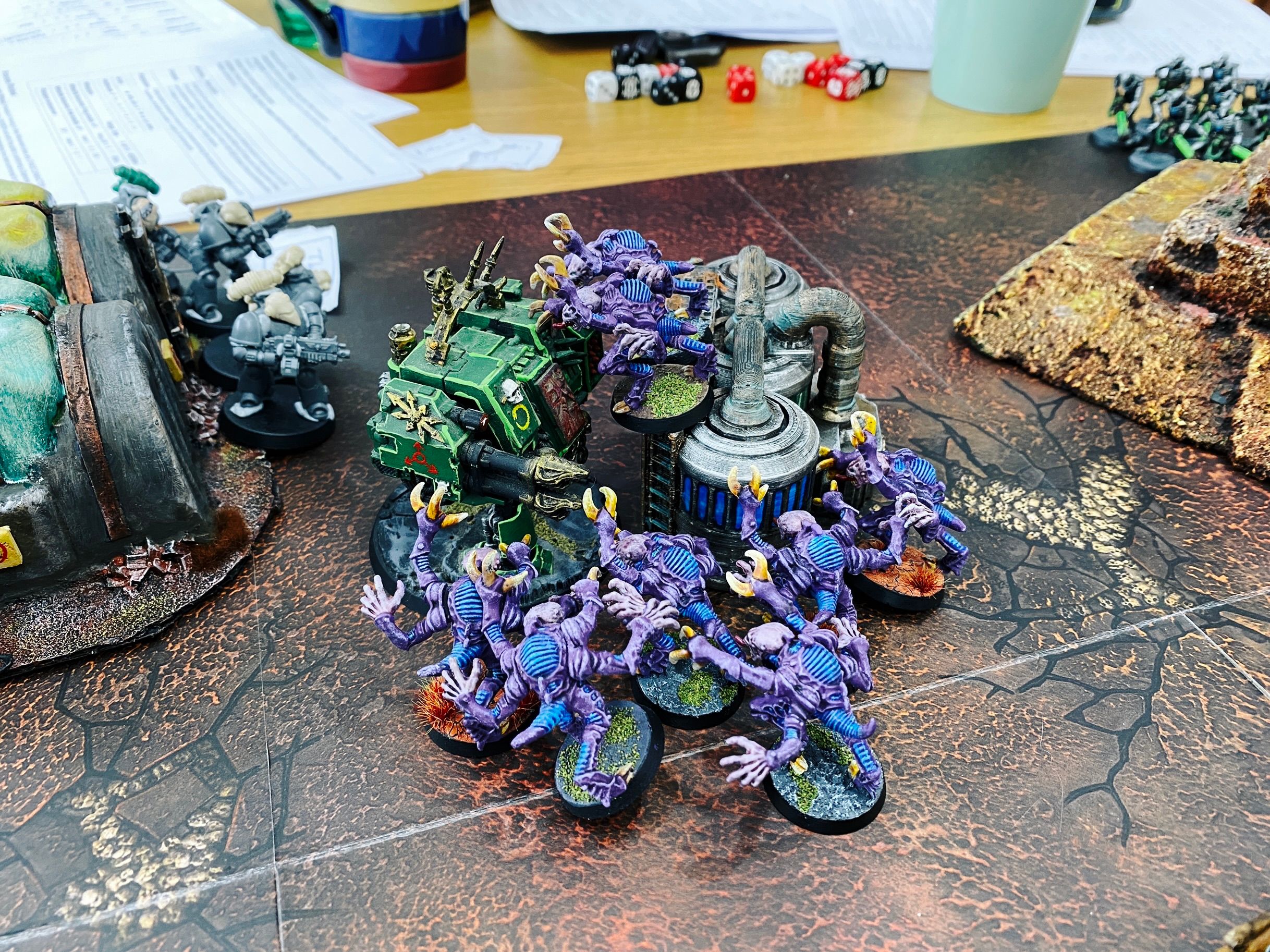 A photo of a big boxy stompy green Chaos Dreadnaught being overrun by eight purple, four-armed Alien-esque Genestealers.
