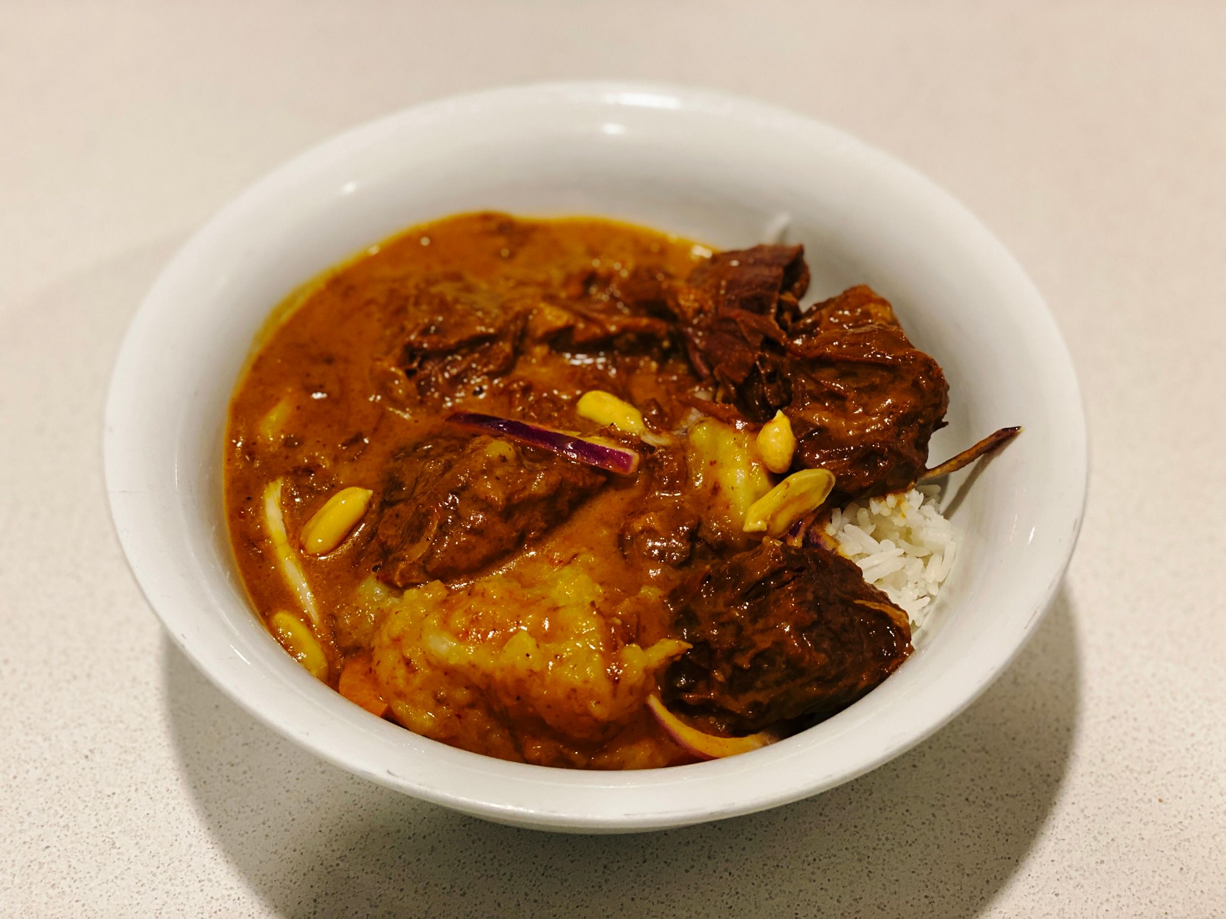 A photo of beef massaman curry on top of rice in a white bowl.