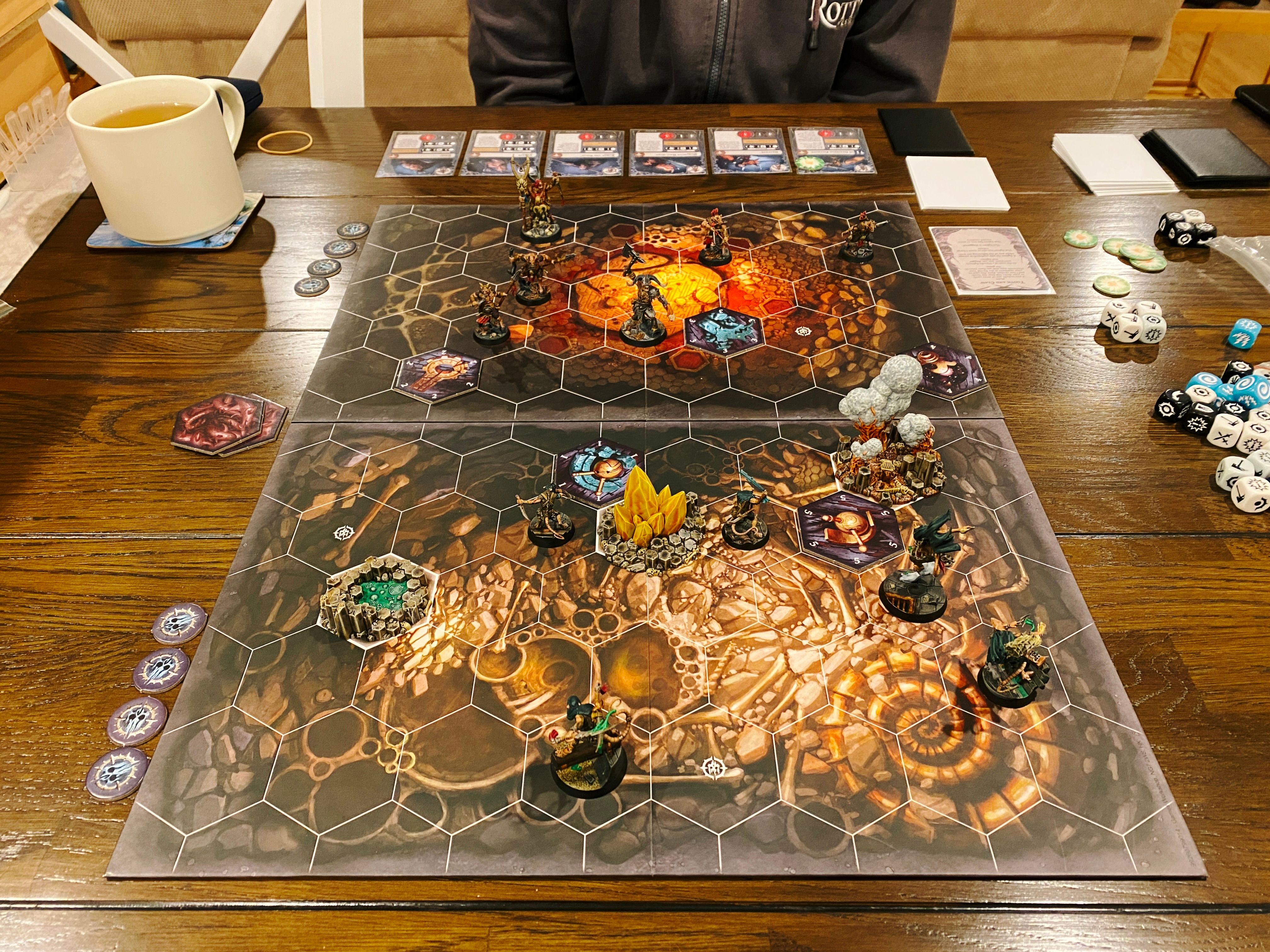 A photo of a Warhammer Underworlds game board. It has hex tiles on it, and the artwork looks like the inside of a cave. Closest to the camera are Skittershank's Clawpack, which consists five ratmen in various dynamic poses (one of them is in the middle of leaping over a smoke bomb he's just set off). At the other end of the board are the six goatmen of Grashrak's Despoilers: two are larger and more intimidating looking, one is holding a giant axe in the air and is gripping the head of someone he just decapitated, and the other four are smaller and shabbier, wielding bows and spears.