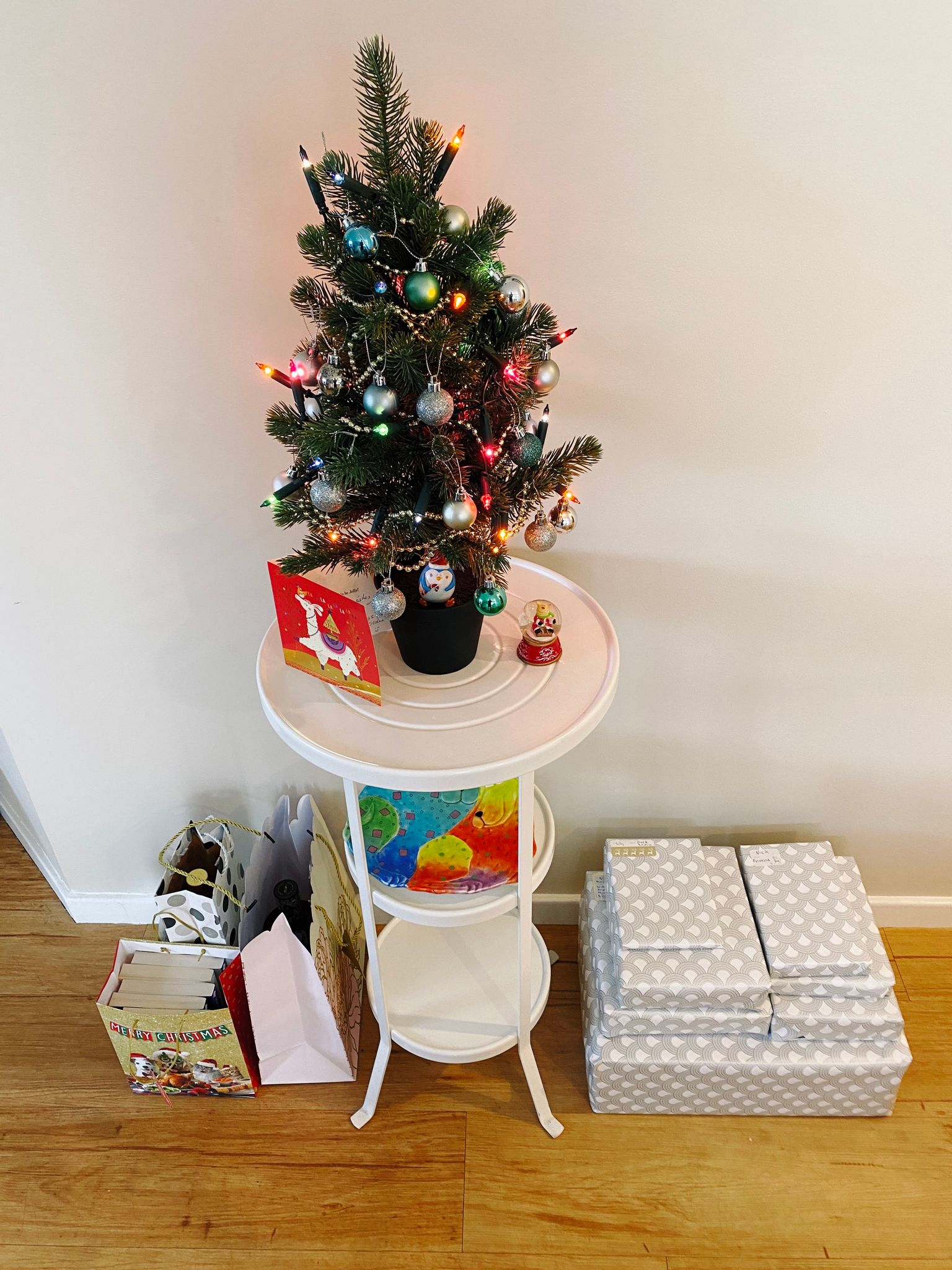 A photo of a small selection of wrapped presents at the base of a white pedestal/stand that has a small decorated Christmas tree on top of it.