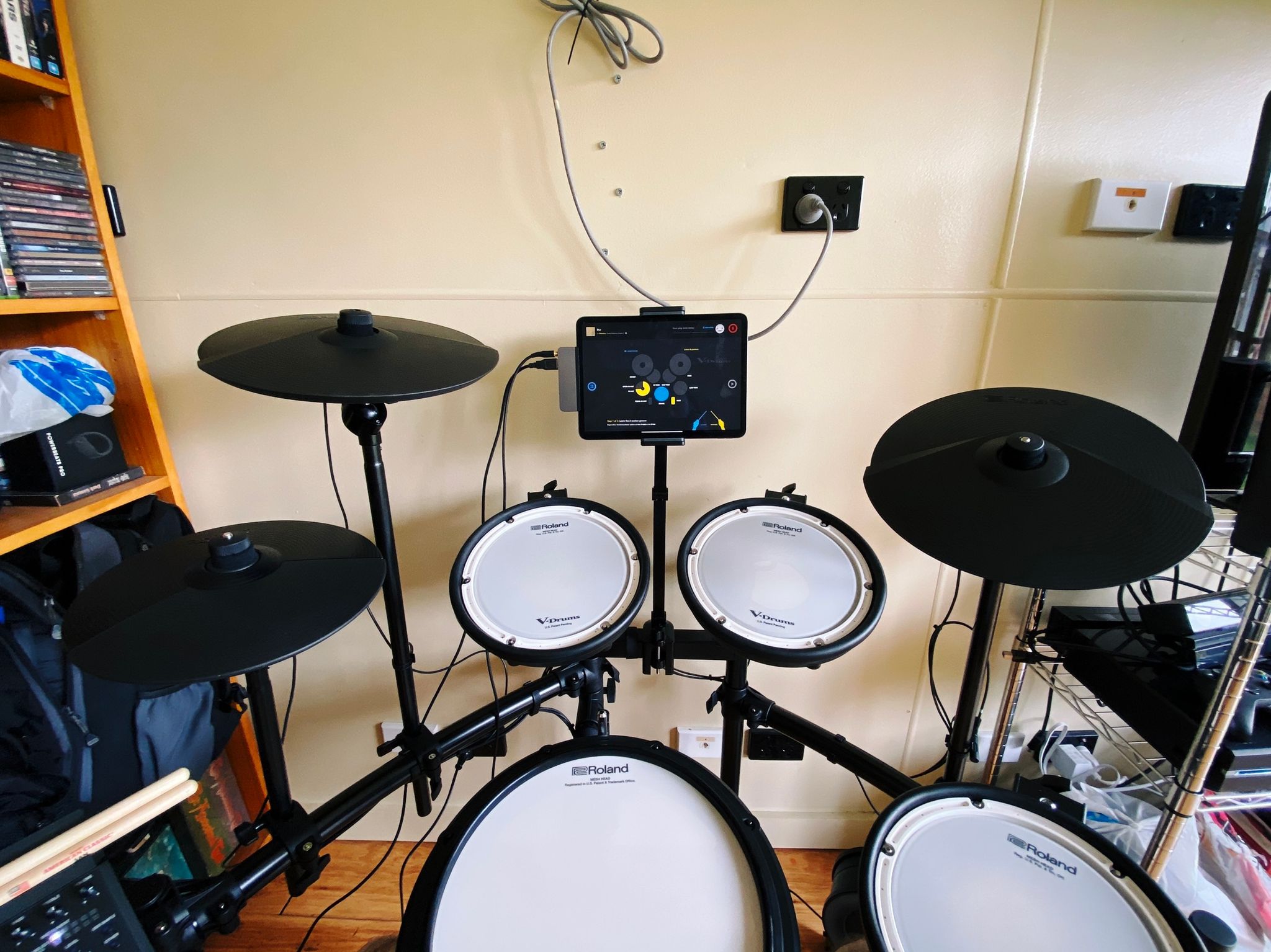 A photo of an electronic drumkit with a metal arm attached to the bar in the middle that's protruding up behind the two middle toms, with an iPad being held at the top of it and the "Melodics" app on screen.