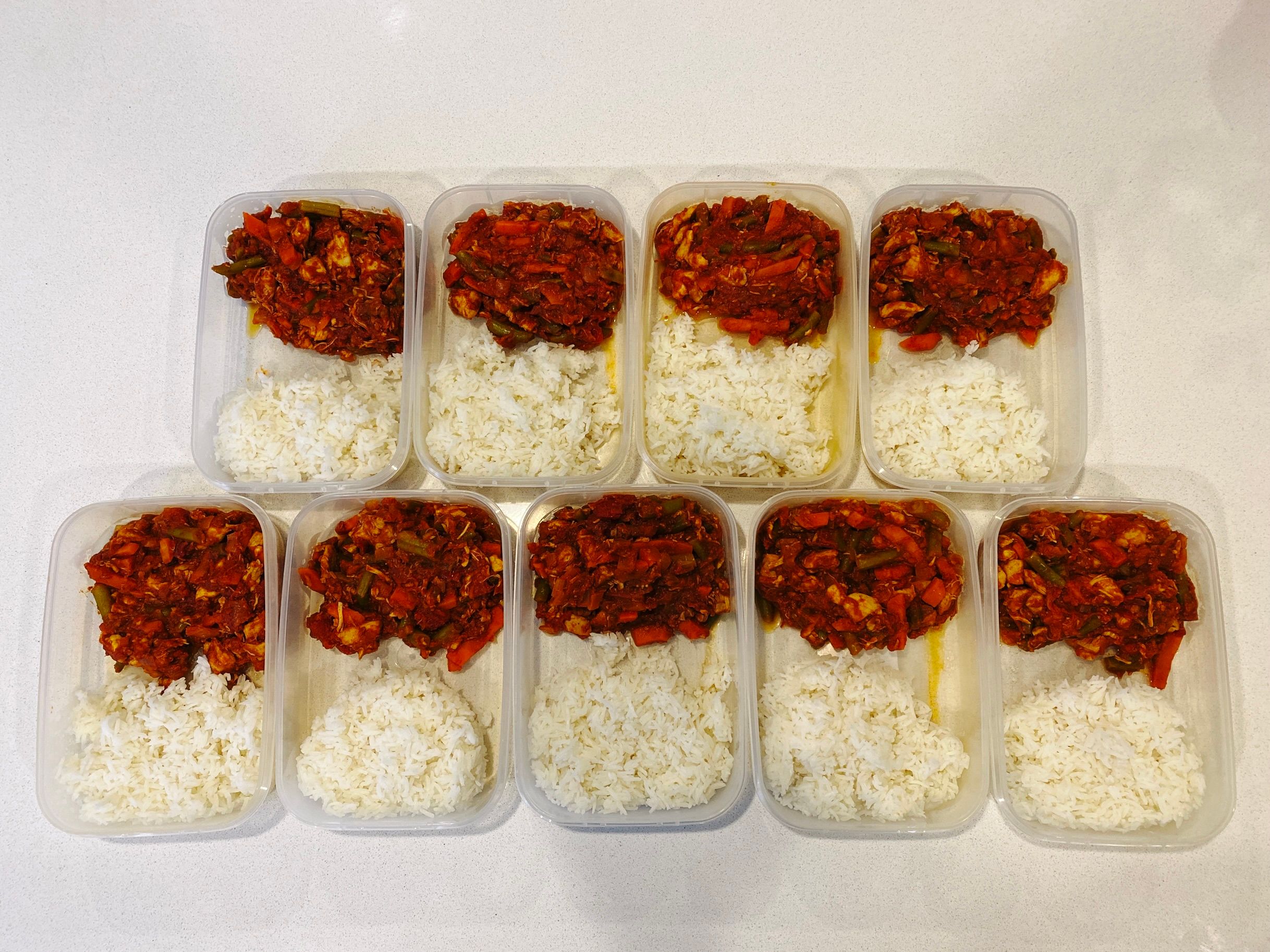 A photo of nine individual tupperware containers that each have half rice and half red tomato-based chicken curry with green beans and carrots in it.