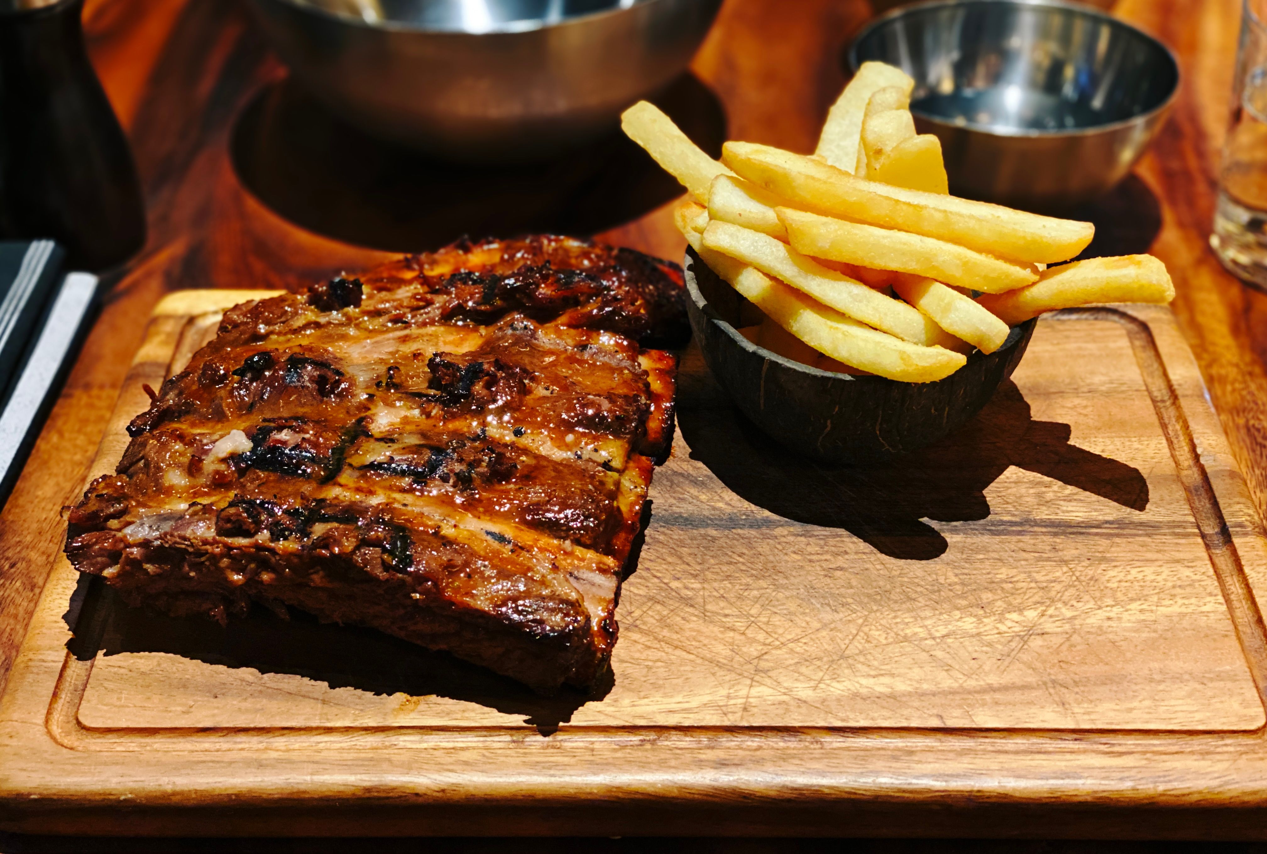 A photo of a half rack of beef ribs and a bowl of chips sitting on a board.