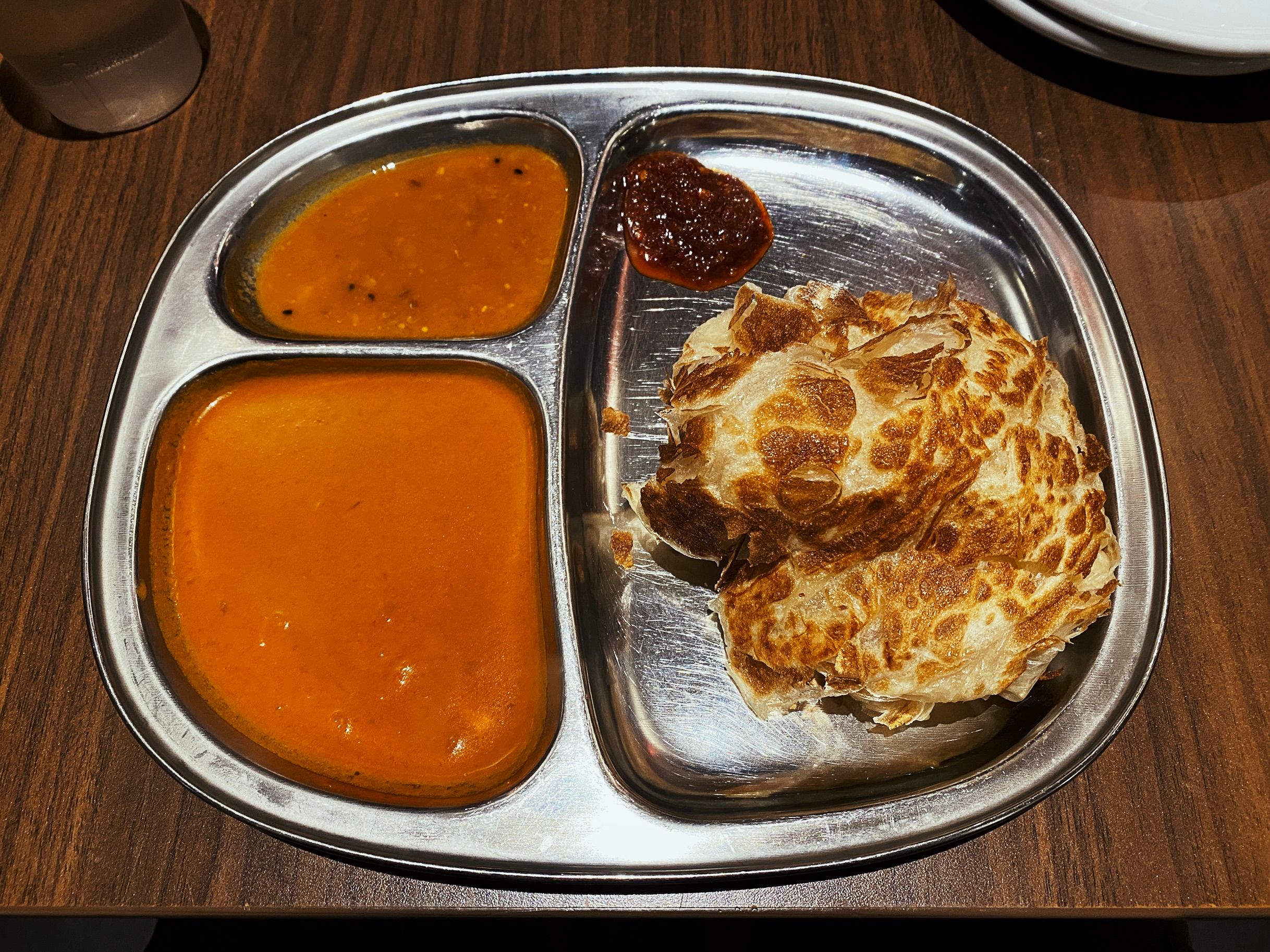 A photo of a roti tisu on a metal tray with two different curry sauces.