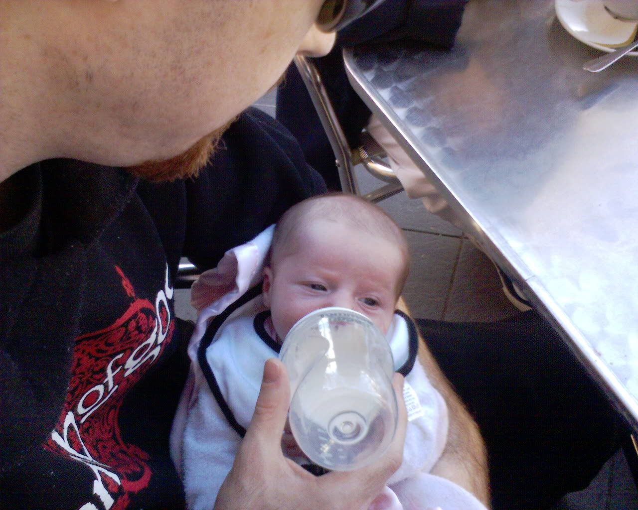 A photo of a tiny newborn baby being fed from a bottle. She's lying in my arms and you can just see the side of my face.