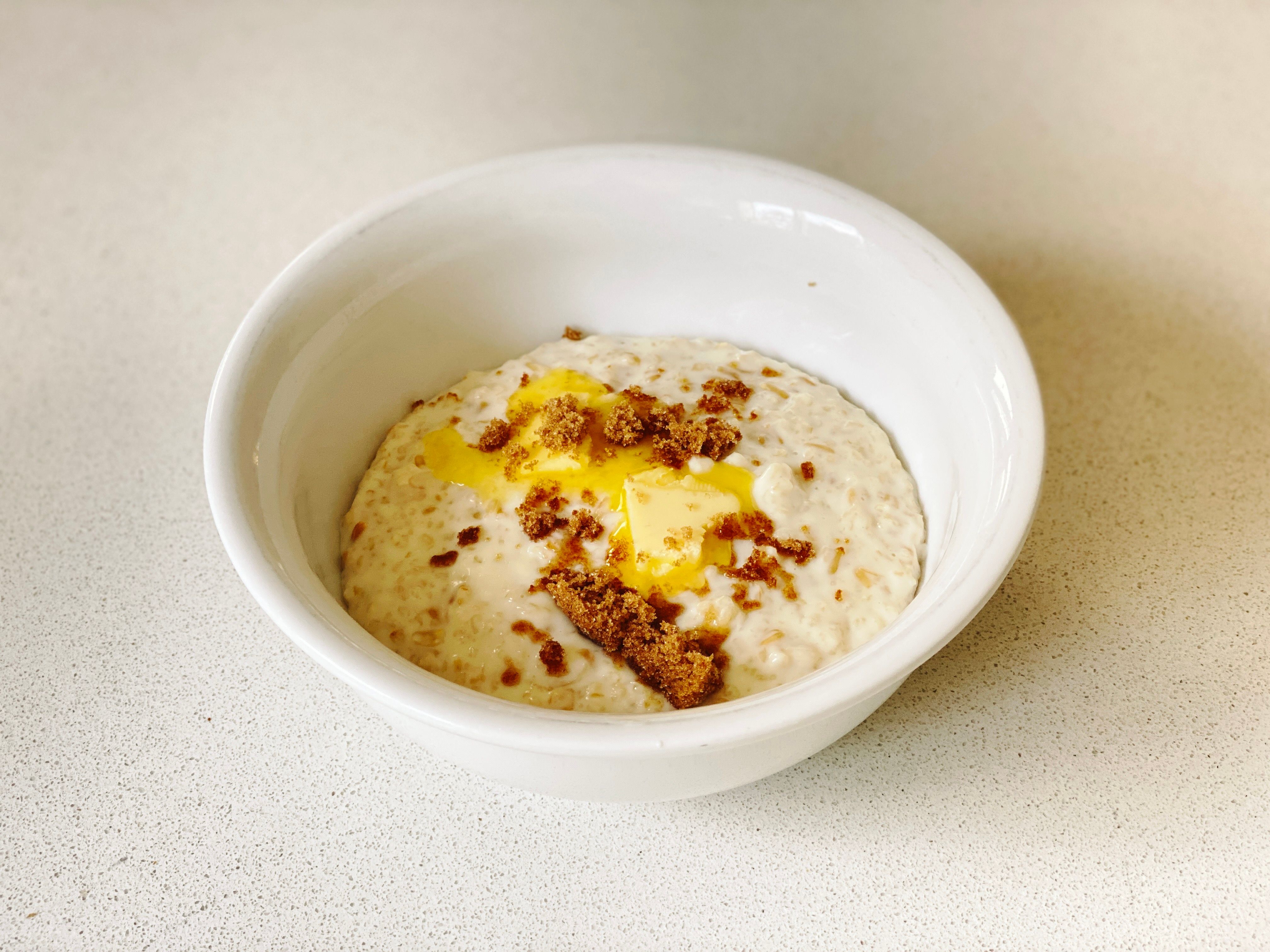 A photo of a bowl of porridge with two slices of butter on top and sprinkled with brown sugar.