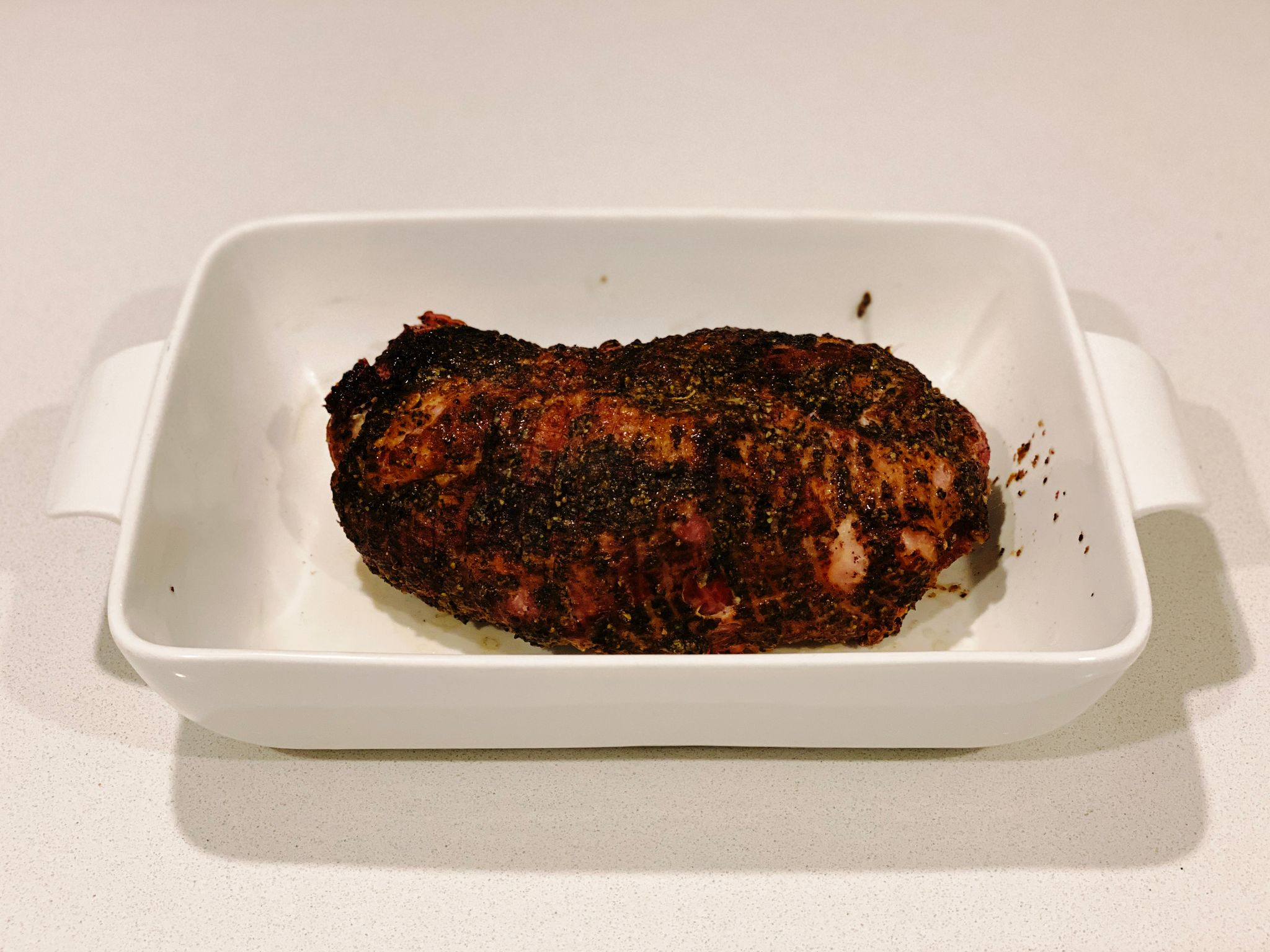 A photo of a hunk of cooked pork covered in pepper and looking delicious.