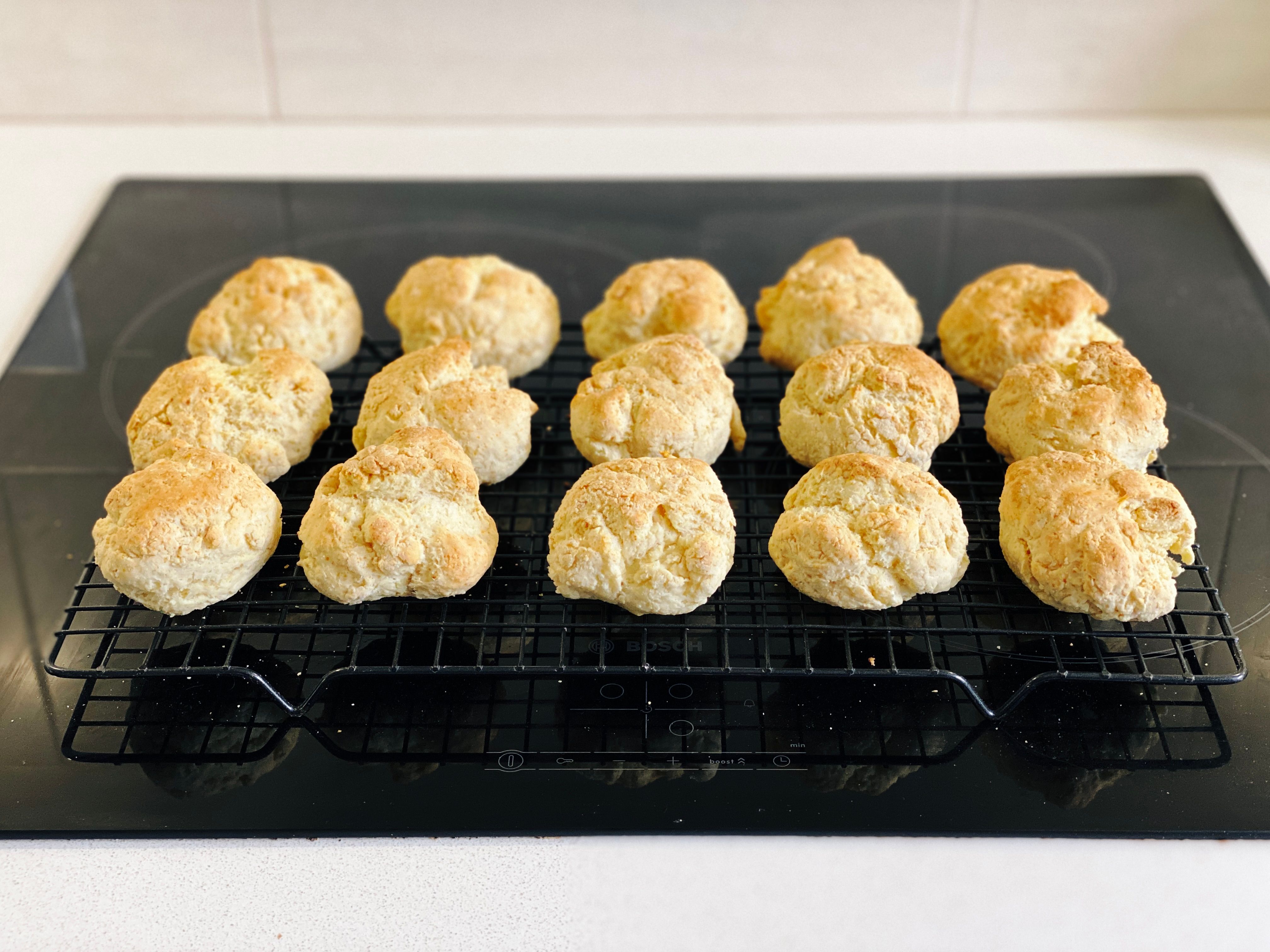 A photo of fifteen golden cut rounds, which look essentially like scones, sitting on a cooling rack.