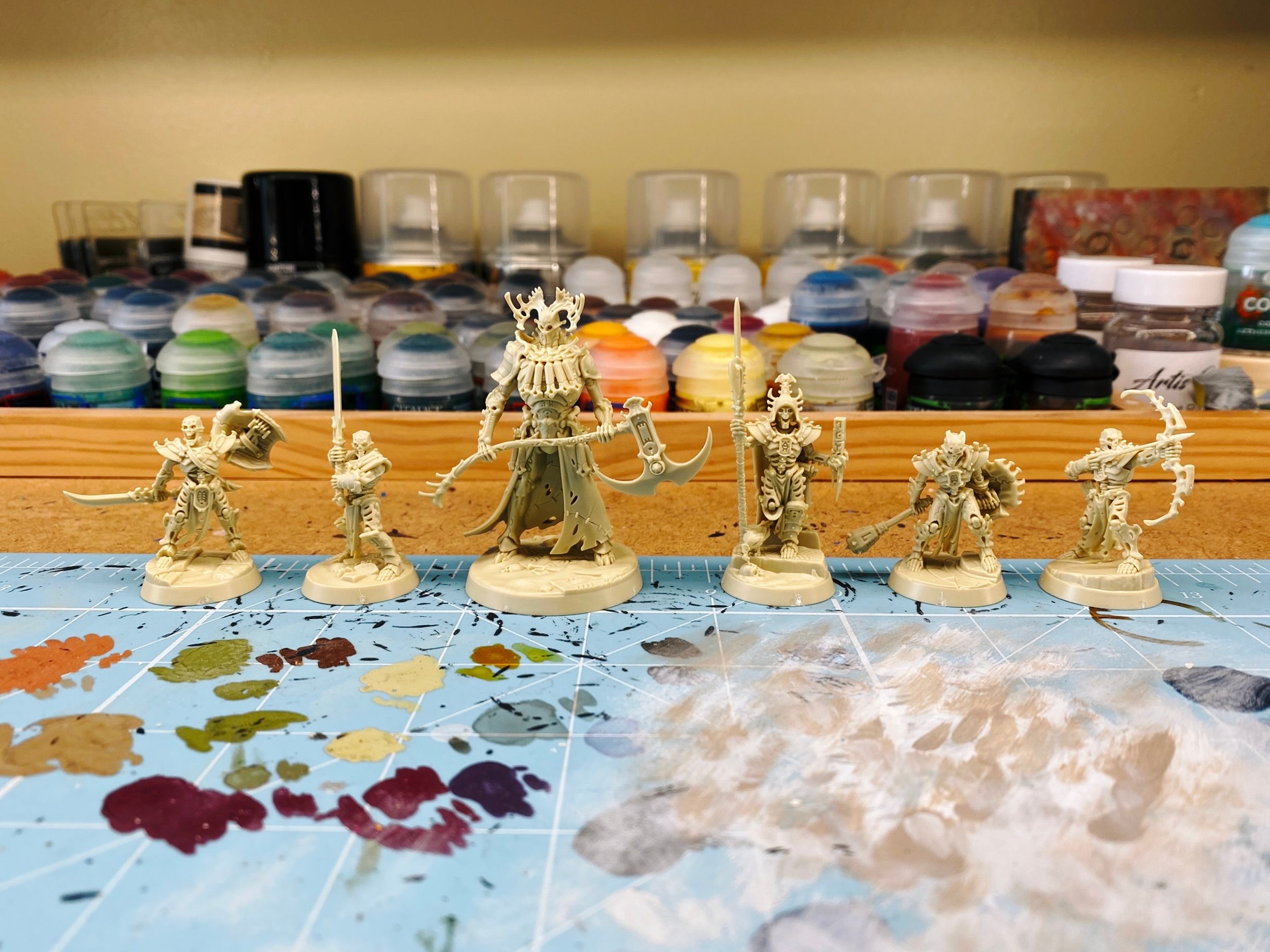 A photo of the Kainan's Reapers warband assembled, in bone-coloured plastic. Six miniatures, all skeletons. Four are warriors holding various weapons, one has a big staff and is weaing an elaborate headdress, and the last is a HUGE armoured fellow towering over the rest, holding a double-bladed scythe.