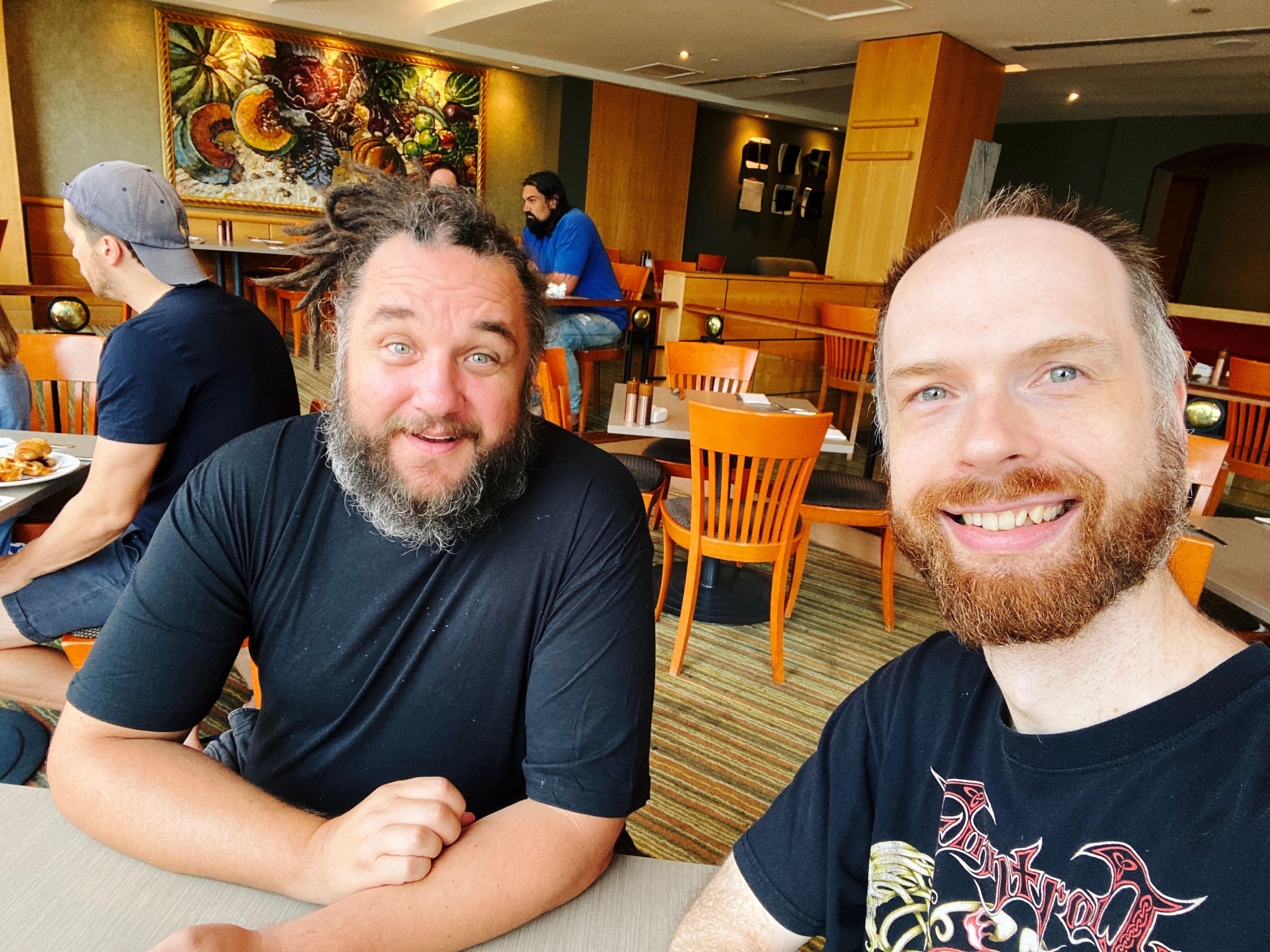 A photo of two white men (me, with a red beard streaked with grey that's getting to be in desperate need of a trim, and my friend who also has a scruffy beard streaked with grey, but his is a very dark brown bordering on black) smiling at the camera.