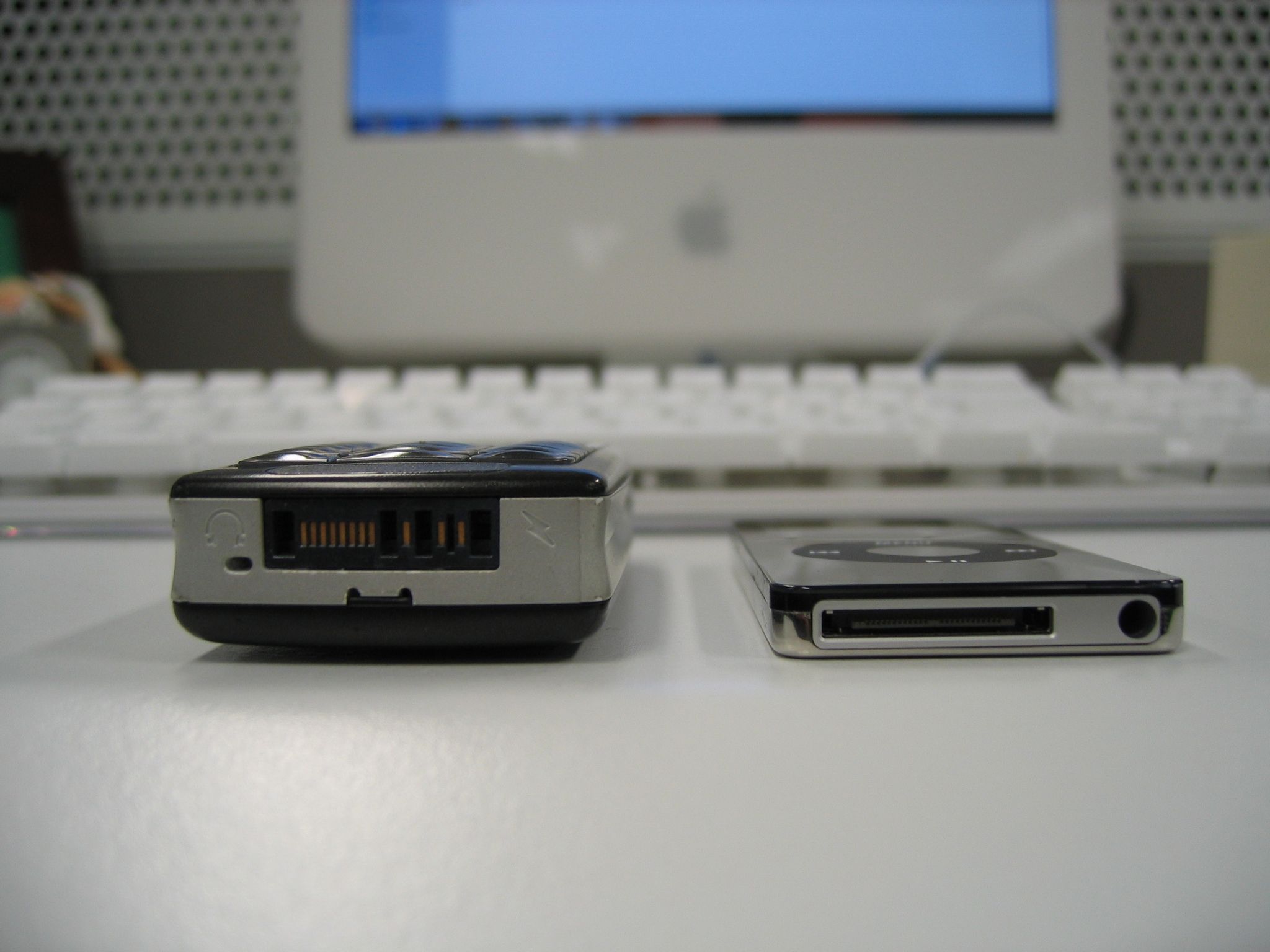 A photo of the bottom of an iPod nano sitting alongside a Sony-Ericsson T630 phone. The phone is HILARIOUSLY thick in comparison to the iPod.