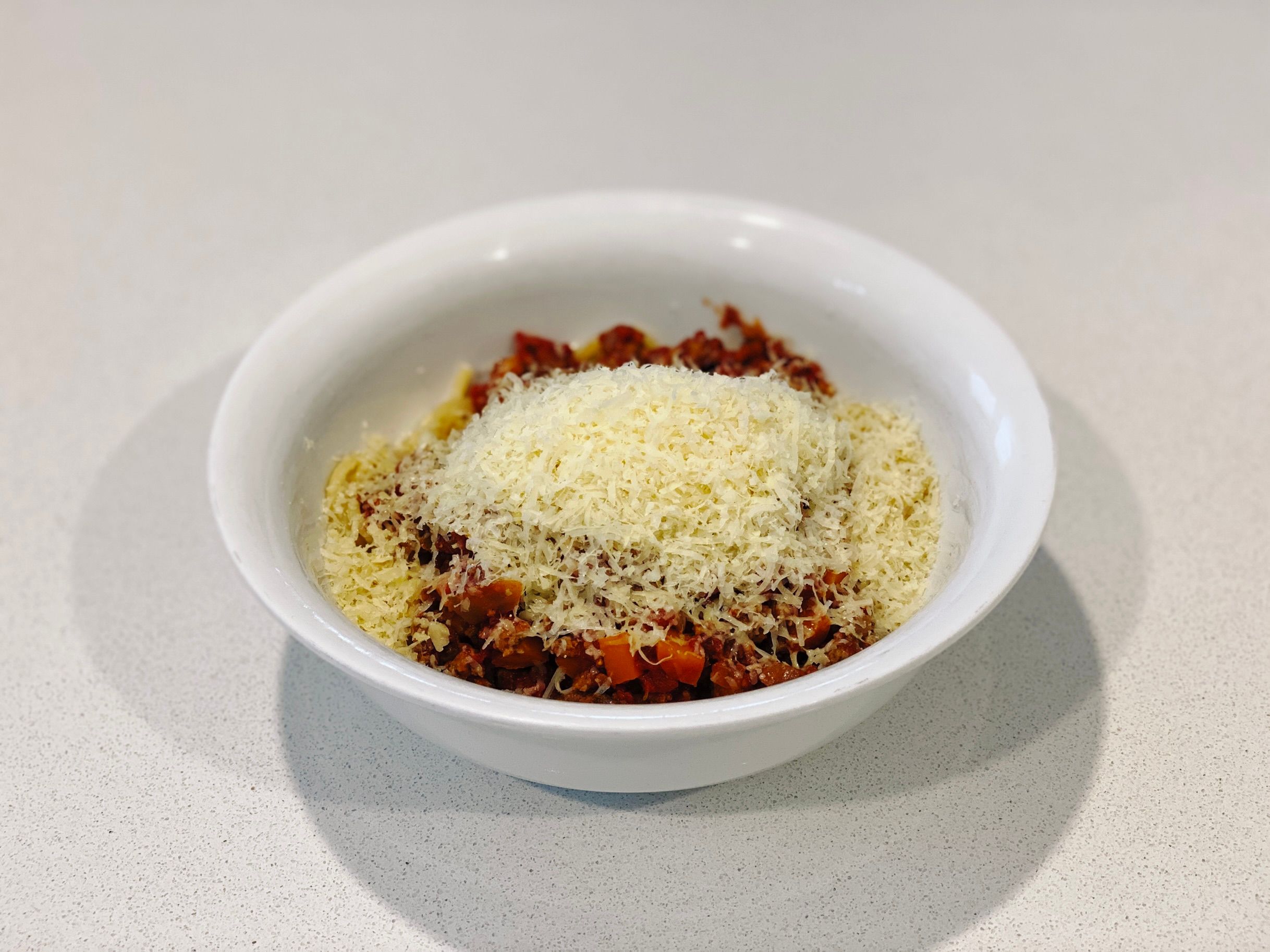 A photo of a bowl of spaghetti with bolognese sauce on top, all covered in grated Parmesan cheese.