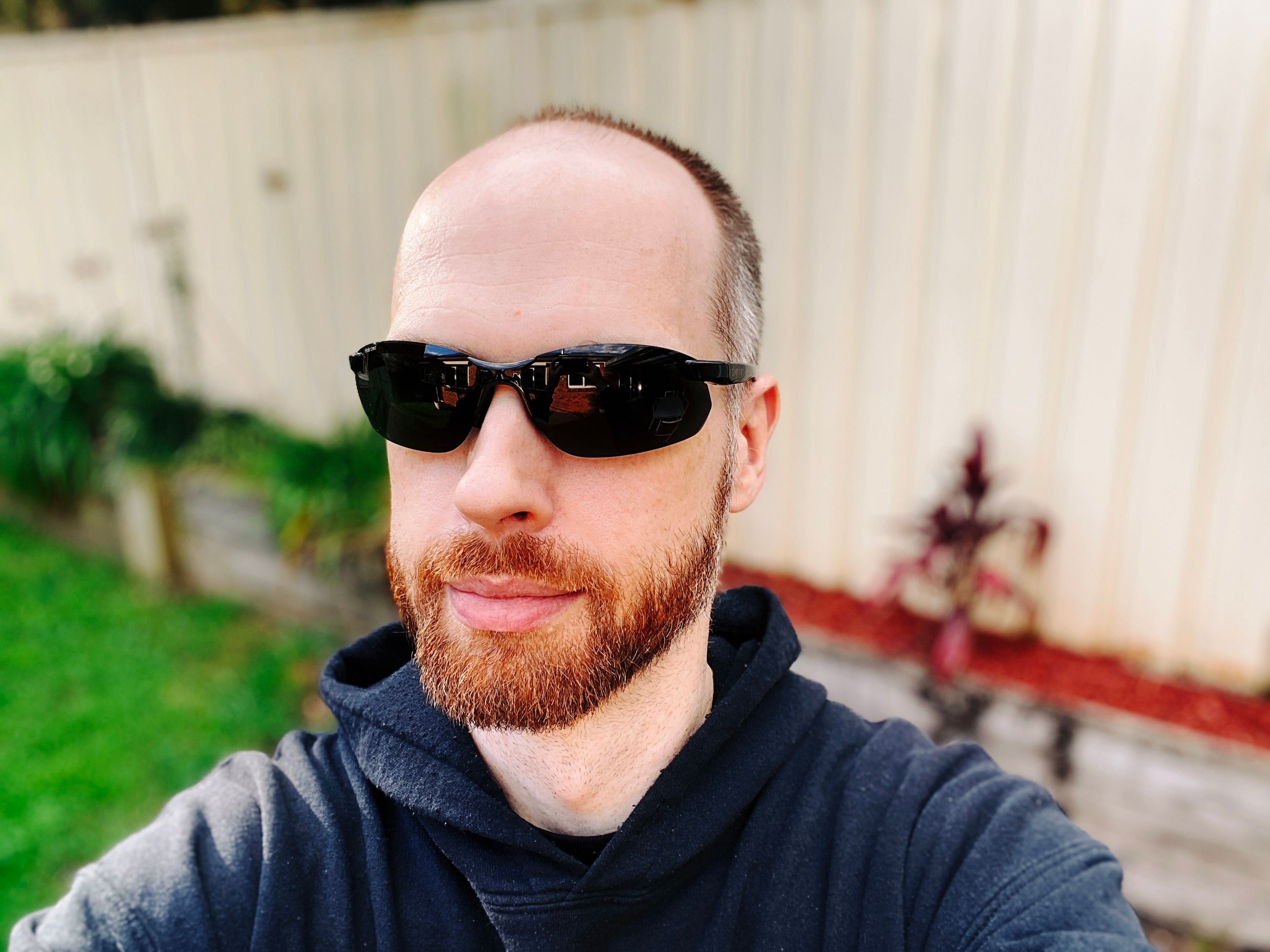 A selfie of me, a white man with a short red beard and short hair, wearing a pair of sleek, dark, frameless sunglasses.