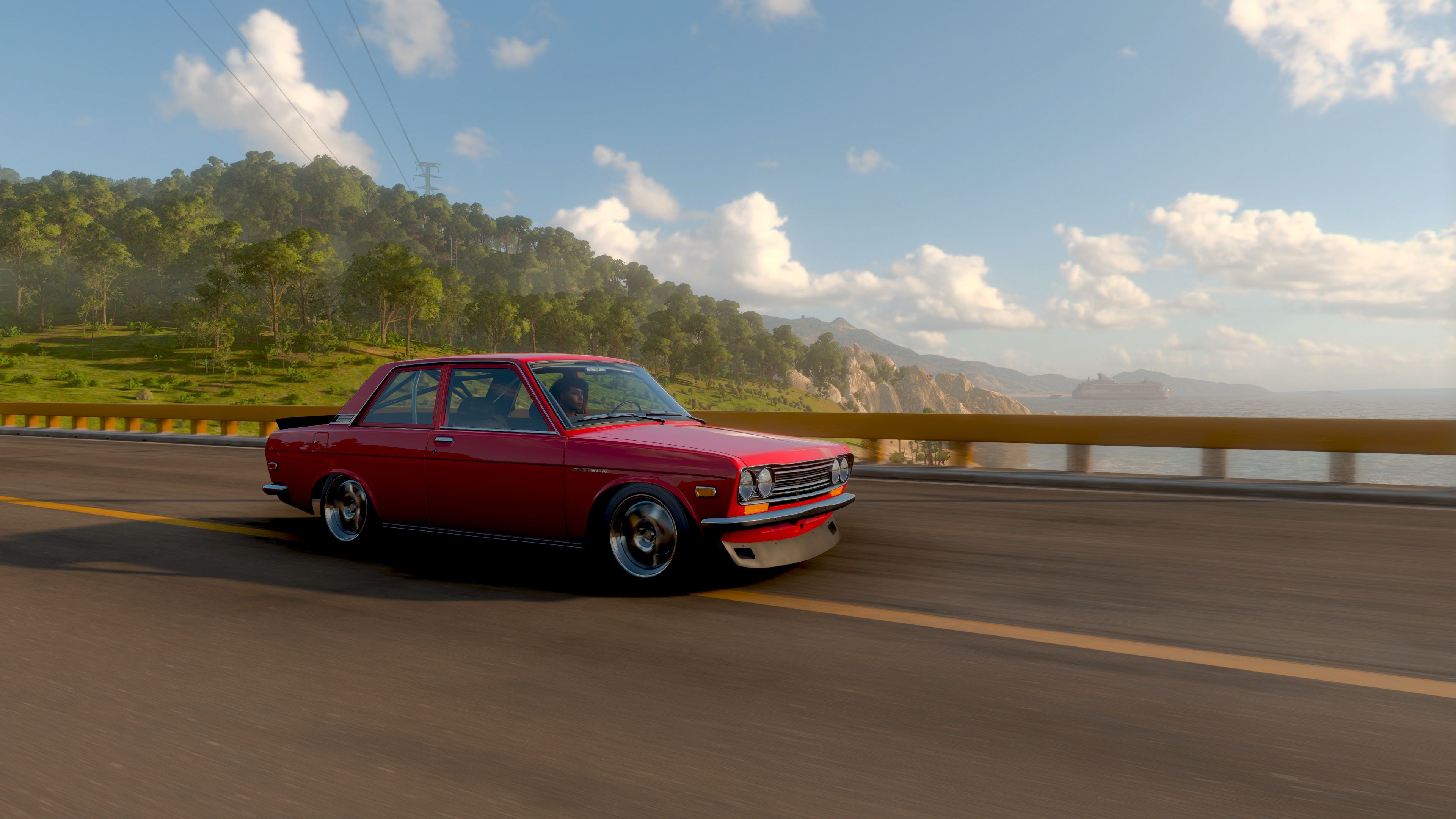 A screenshot from Forza Horizon 5, it's a three-quarter-profile action shot of my red Datsun that's been lowered and has sweet-looking rims on it driving across a bridge. The sky is blue with fluffy clouds, and there's bright green trees over the shoreline behind the bridge.