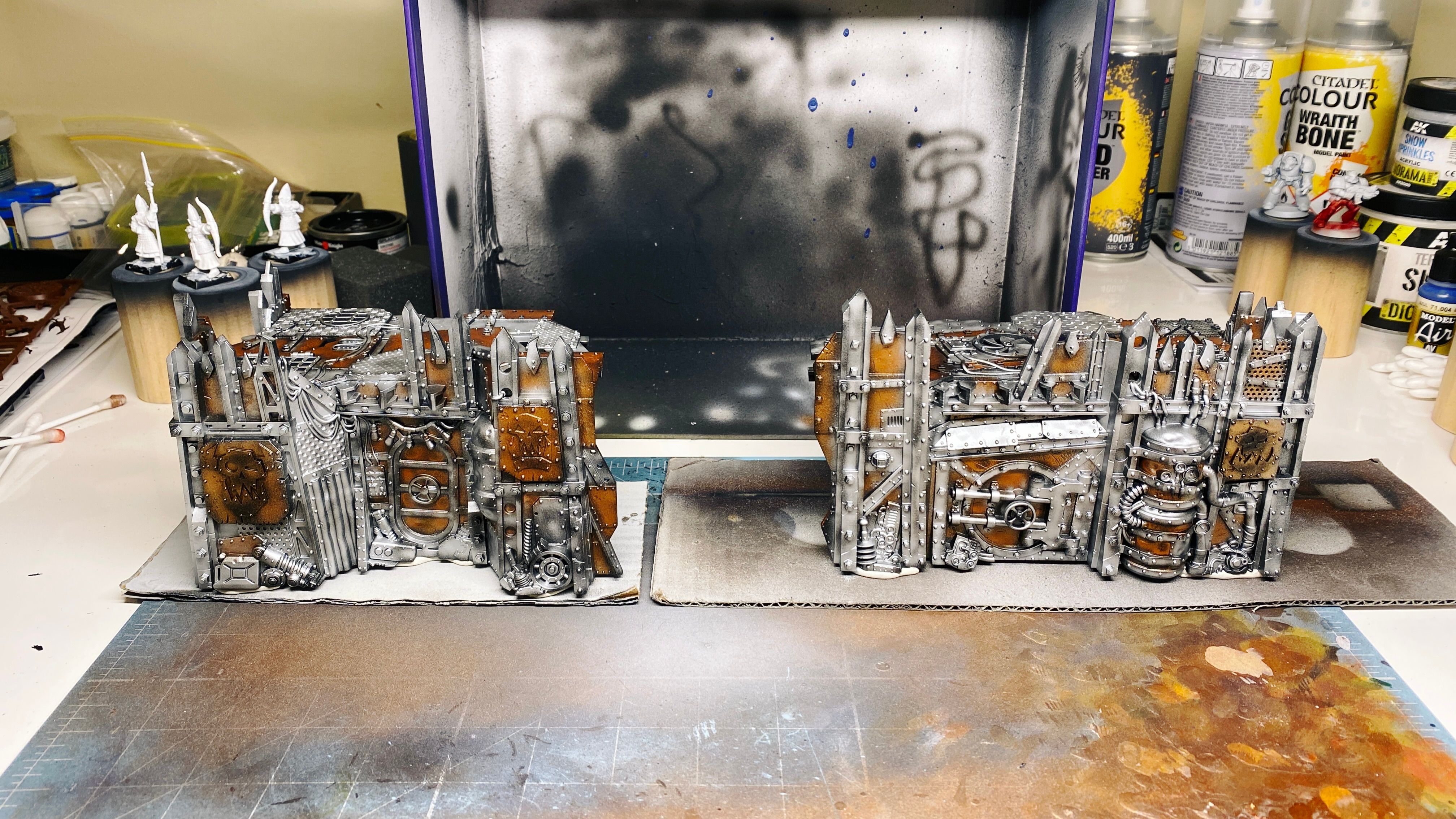 Two pieces of Warhammer 40,000: Kill Team terrain. They're parts of an Ork fort and look like they belong in a junk yard, the walls and platform on top are made up of a whole ton of pieces of metal scrap, like big plates, corrugated pieces, massive beams, there's a door in there, and a couple of empty gas cylinders. They're EXTREMELY ramshackle.