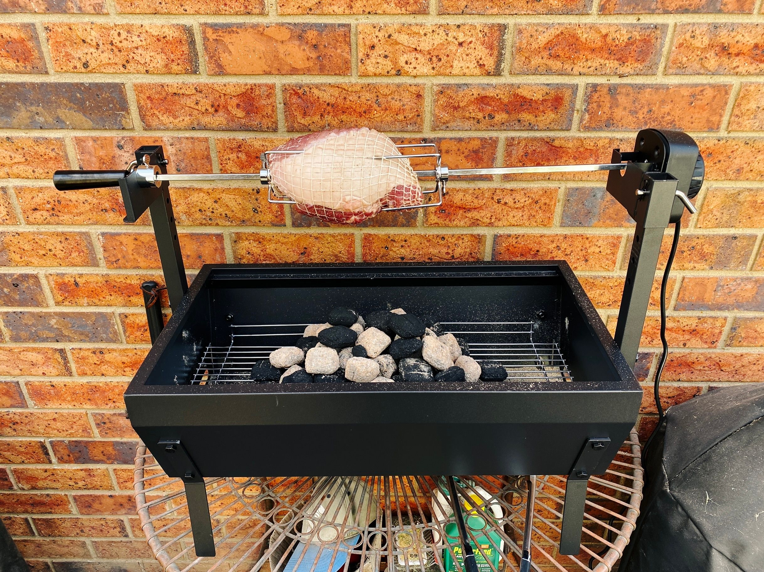 A photo of a small rolled pork shoulder on a spit roaster.