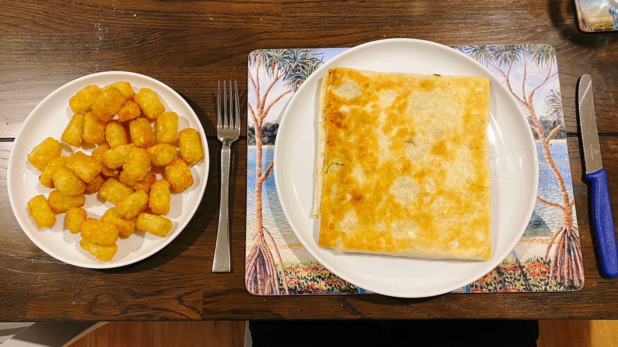 A photo of a dinner plate with a big square gozleme in it, with a small plate next to it filled with potato gems.