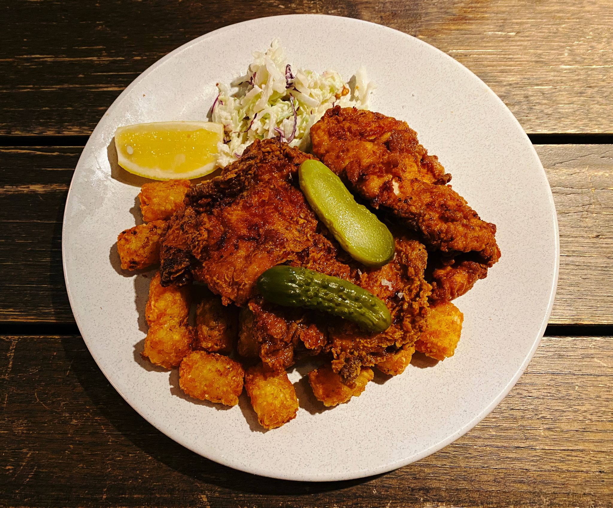 A photo of a plate of Southern fried chicken on top of potato gems with slaw on the side.