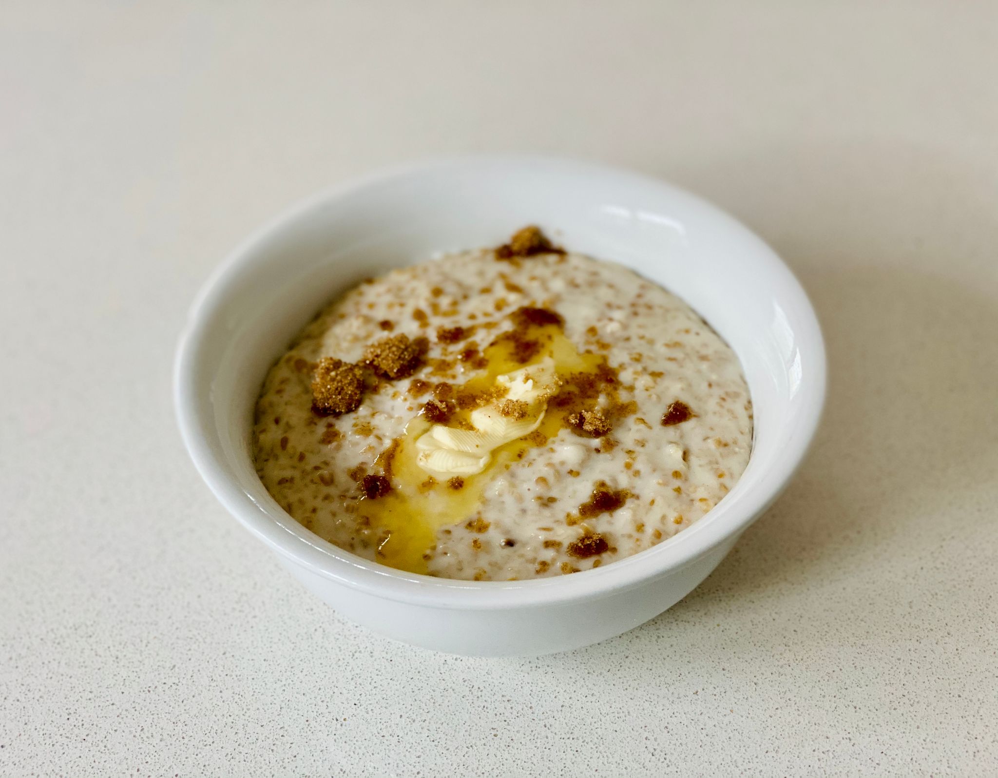 A photo of a bowl of porridge topped with a dollop of butter and a sprinkling of brown sugar.