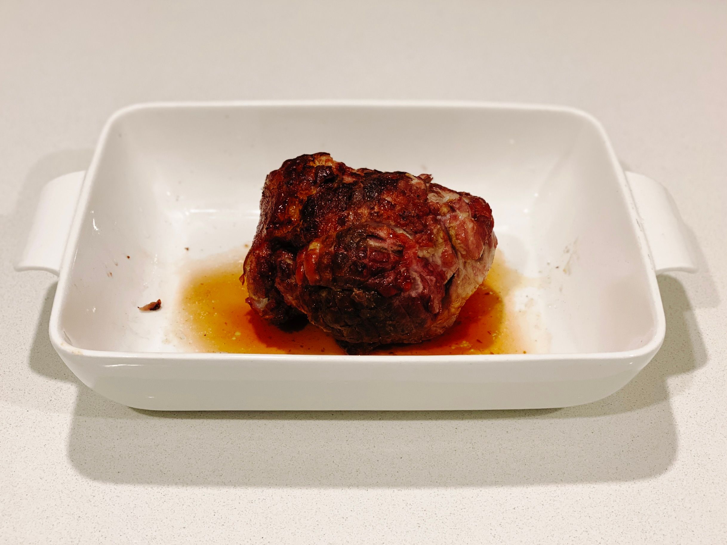 A photo of a small cooked pork roast sitting in a white casserole dish.