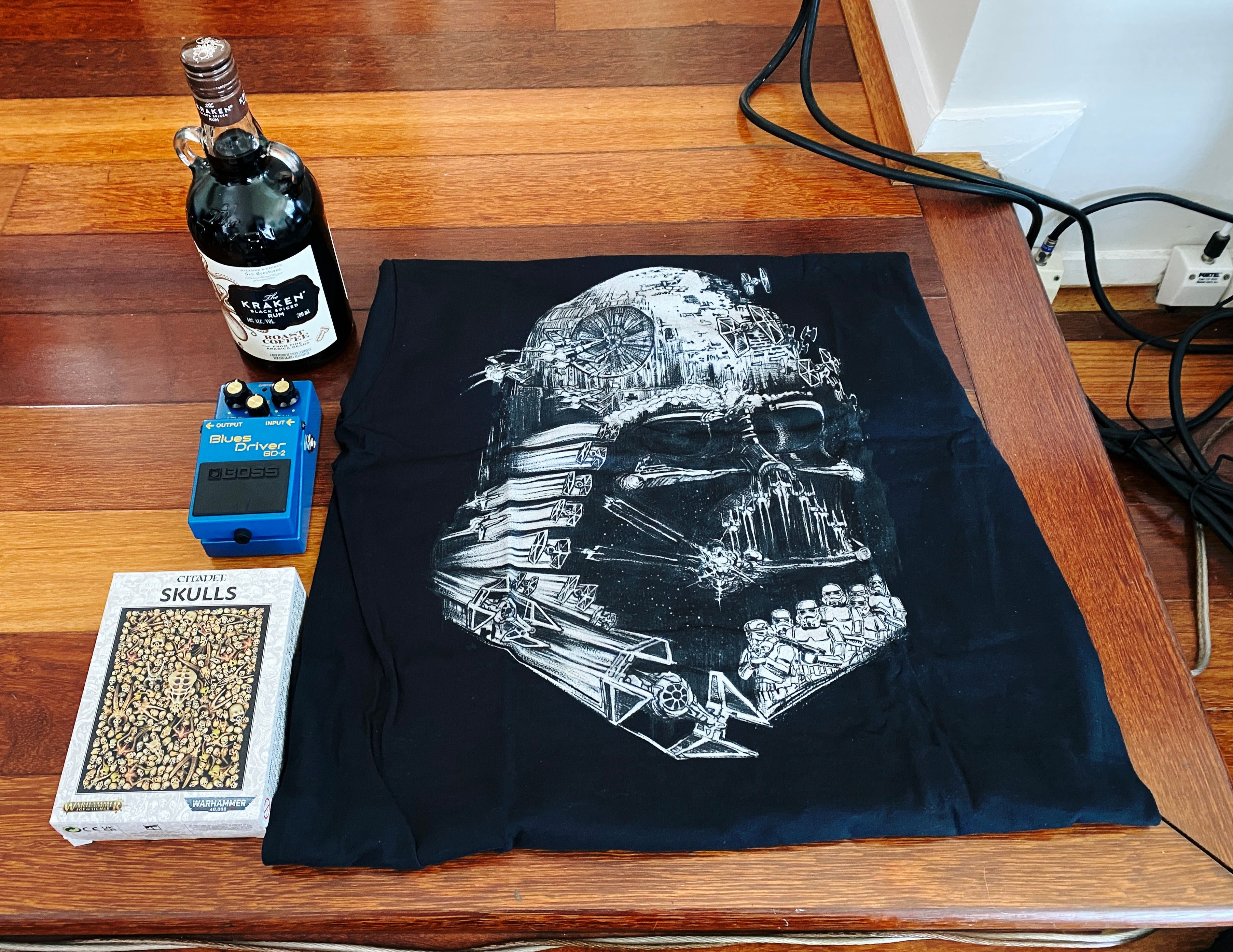 A photo of a bottle of Kraken spiced roast coffee rum, a Boss "Blues Driver" guitar pedal, a box of 300 miniature skulls for decorating my various Games Workshop miniature bases, and a black t-shirt with a dark on the front that looks like Darth Vader but he's made up of the Death Star and Storm Troopers and TIE Fighters.