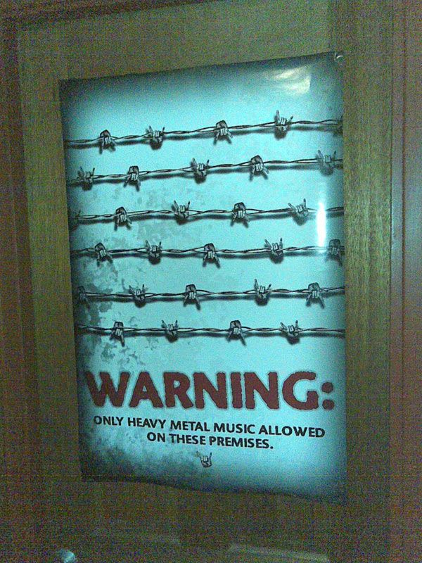 A poster on a door. There's six barbed wire segments going across horizontally, except where the barbs would be are hands throwing the horns. Underneath it says "WARNING: Only heavy metal music allowed on these premises."