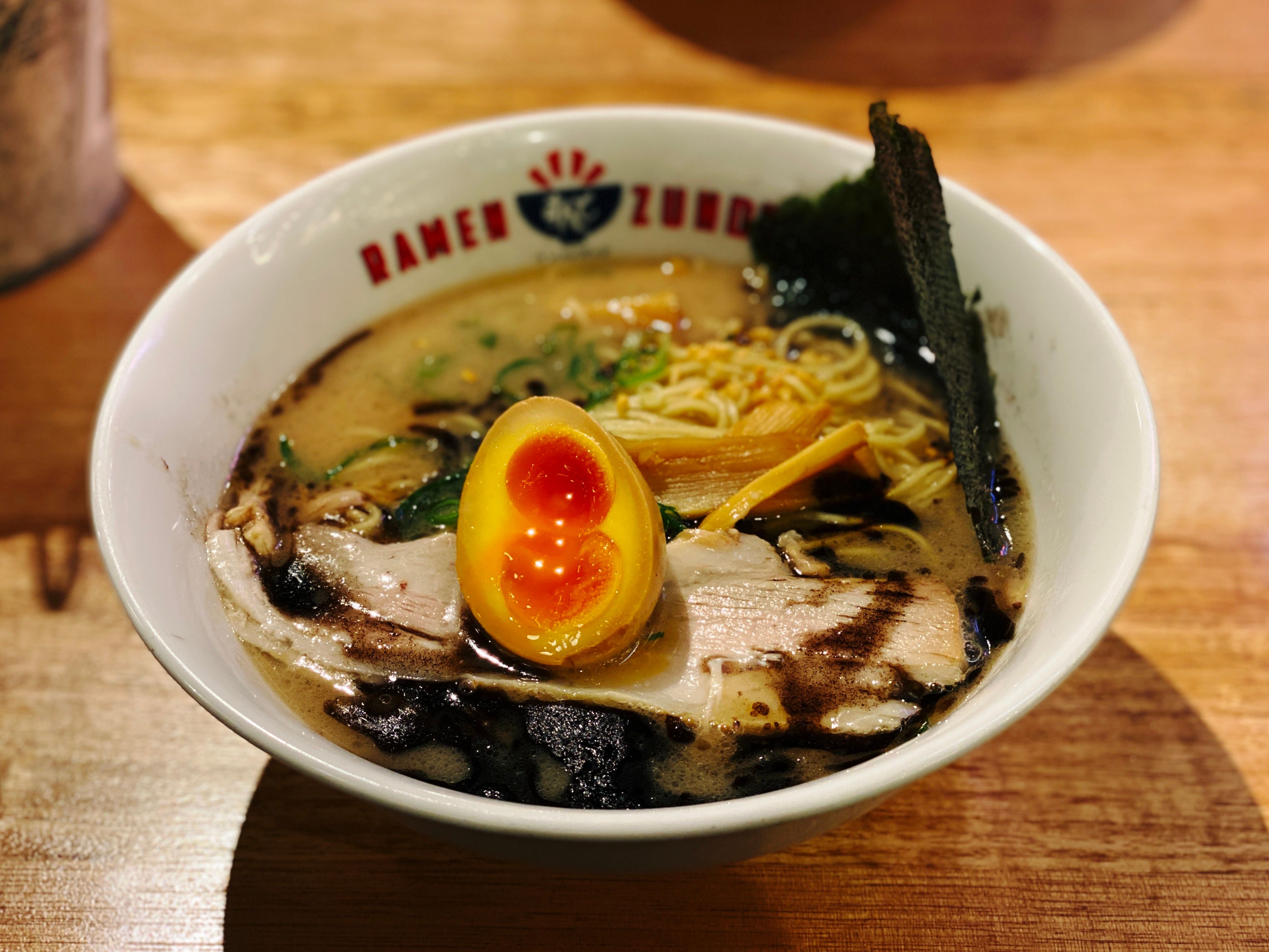 A photo of a bowl of ramen with a slice of pork in it, and half a boiled egg sitting on top.