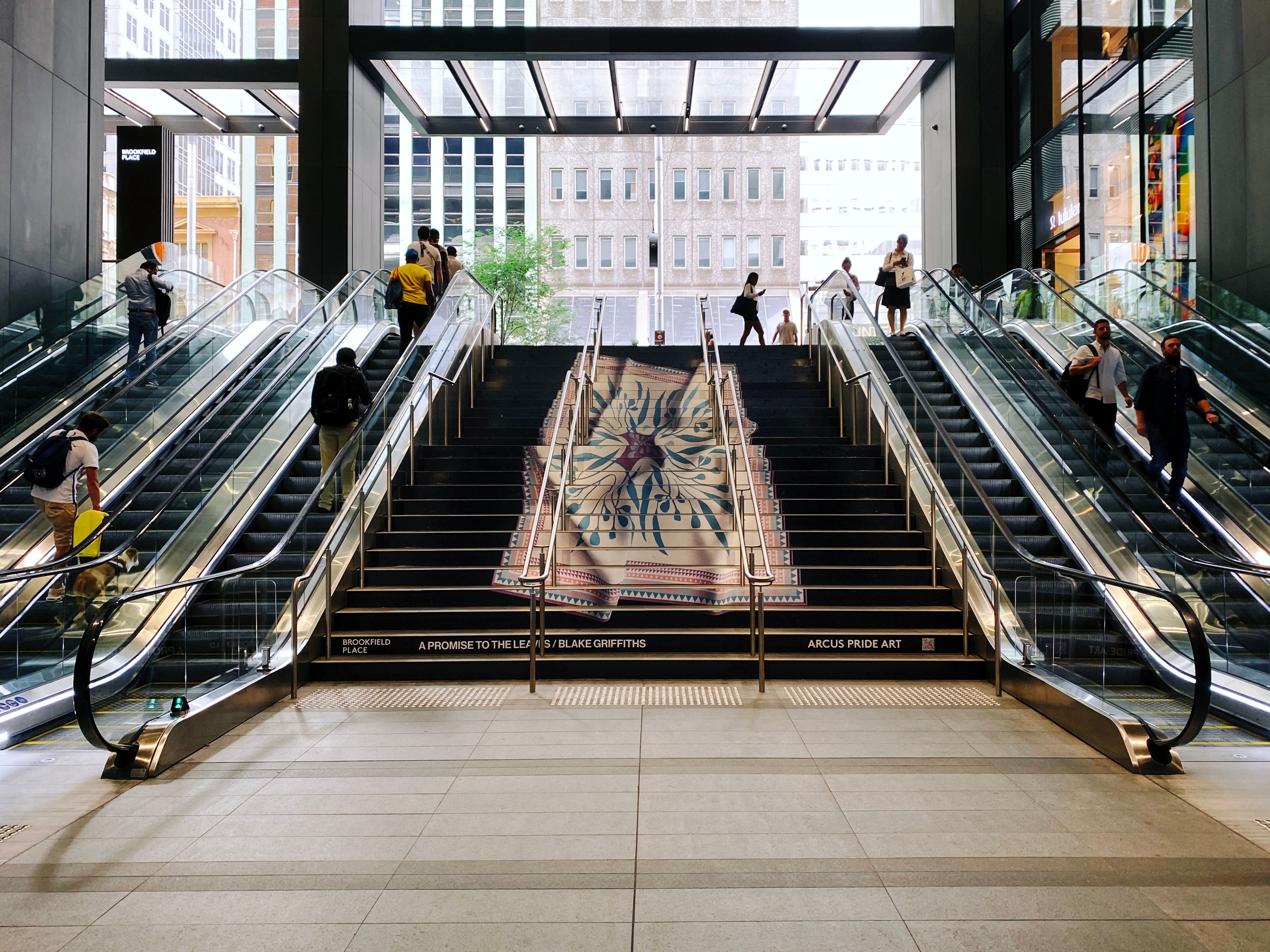 A photo of a wide set of stairs leading upwards where the front face of each of the steps has part of a piece of art on it. The art itself looks like a big carpet with a native flower design on it, and the whole thing has wavy parts in it like it's blowing in the wind.