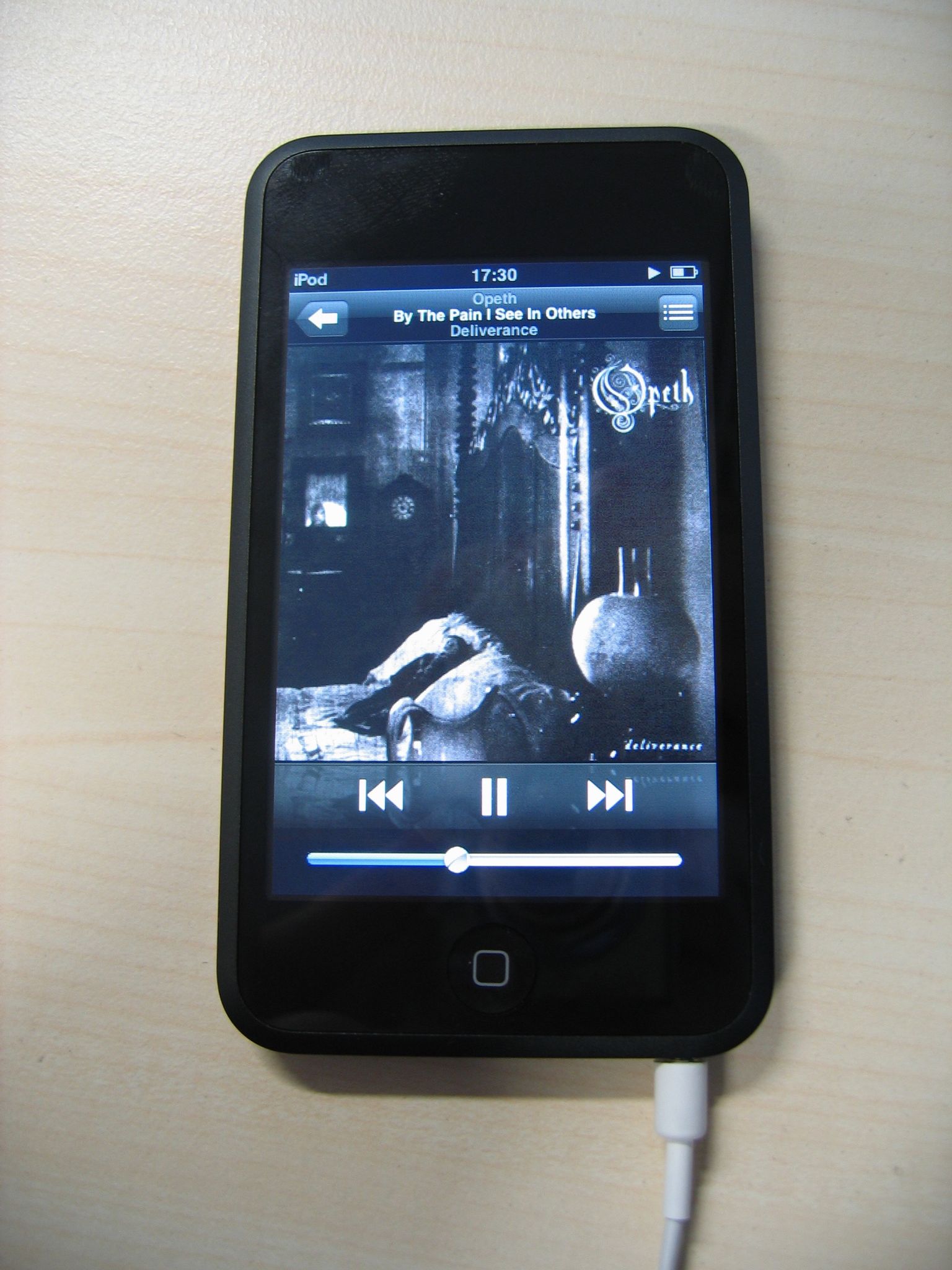 A photo of a black iPod touch with the standard white iPod earbuds plugged in, playing the song "By The Pain I See In Others" by Opeth.
