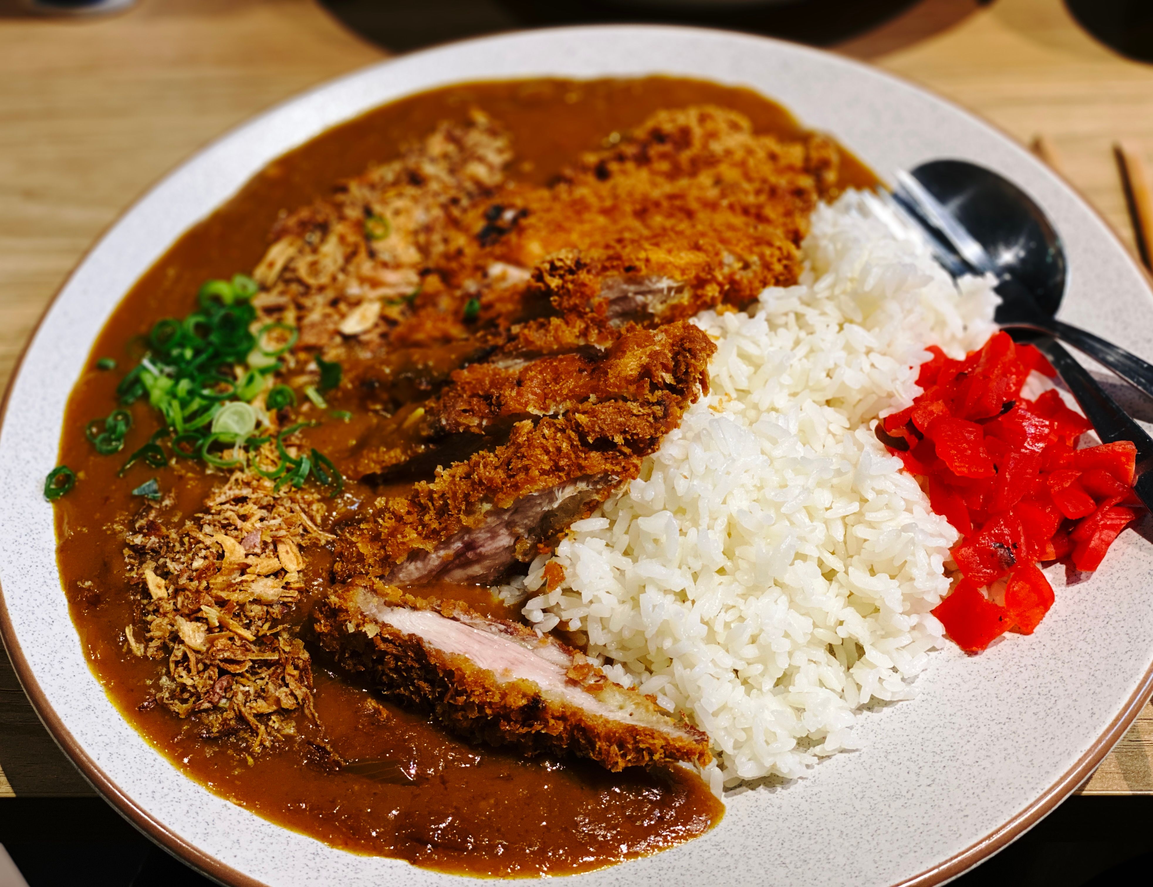 A very large plate half covered in a thick brown sauce, with rice and sliced up fried chicken on the other side.