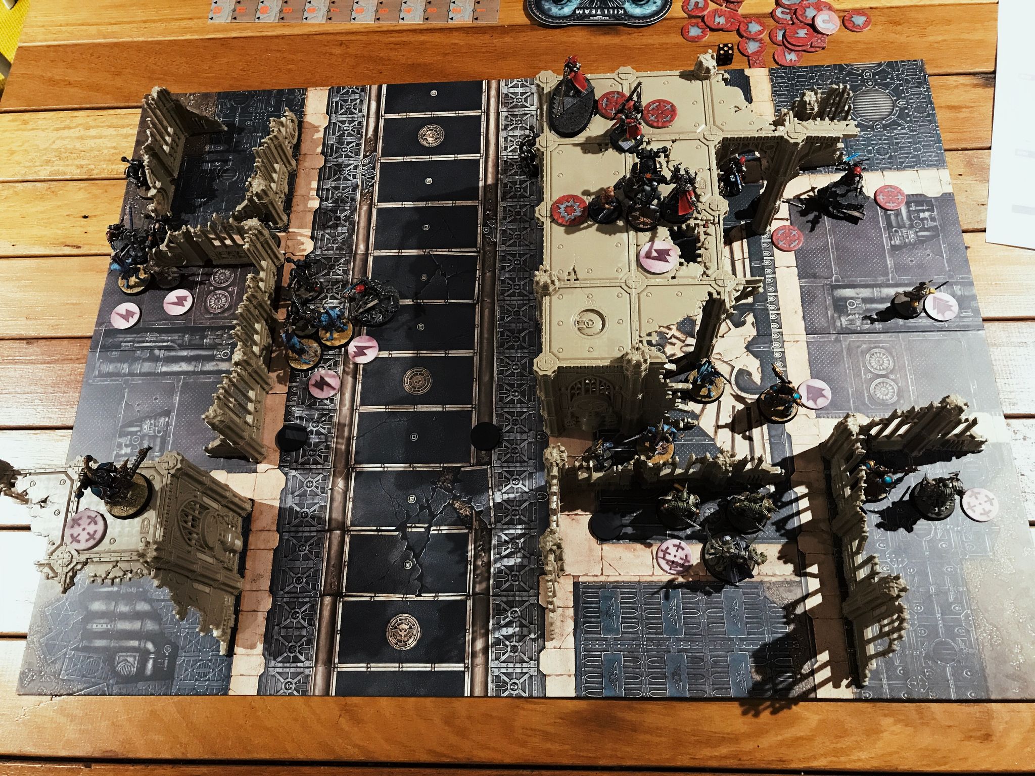 A photo from above a Warhammer 40K Kill Team battle. Miniatures are all over the board and there's plastic building ruins in it.